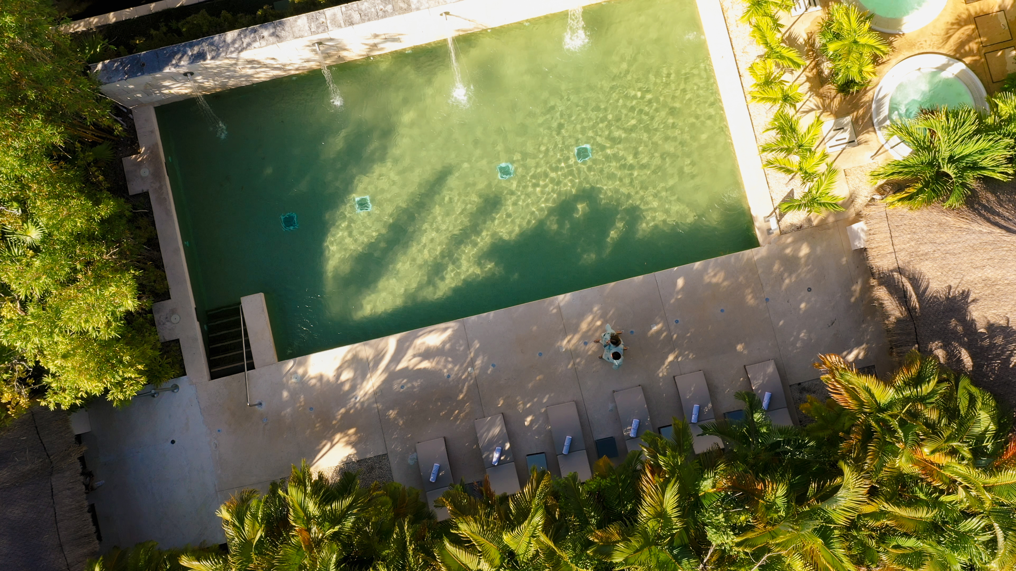 Resort swimming pool aerial view with lounge chairs, fountains, and palm trees.