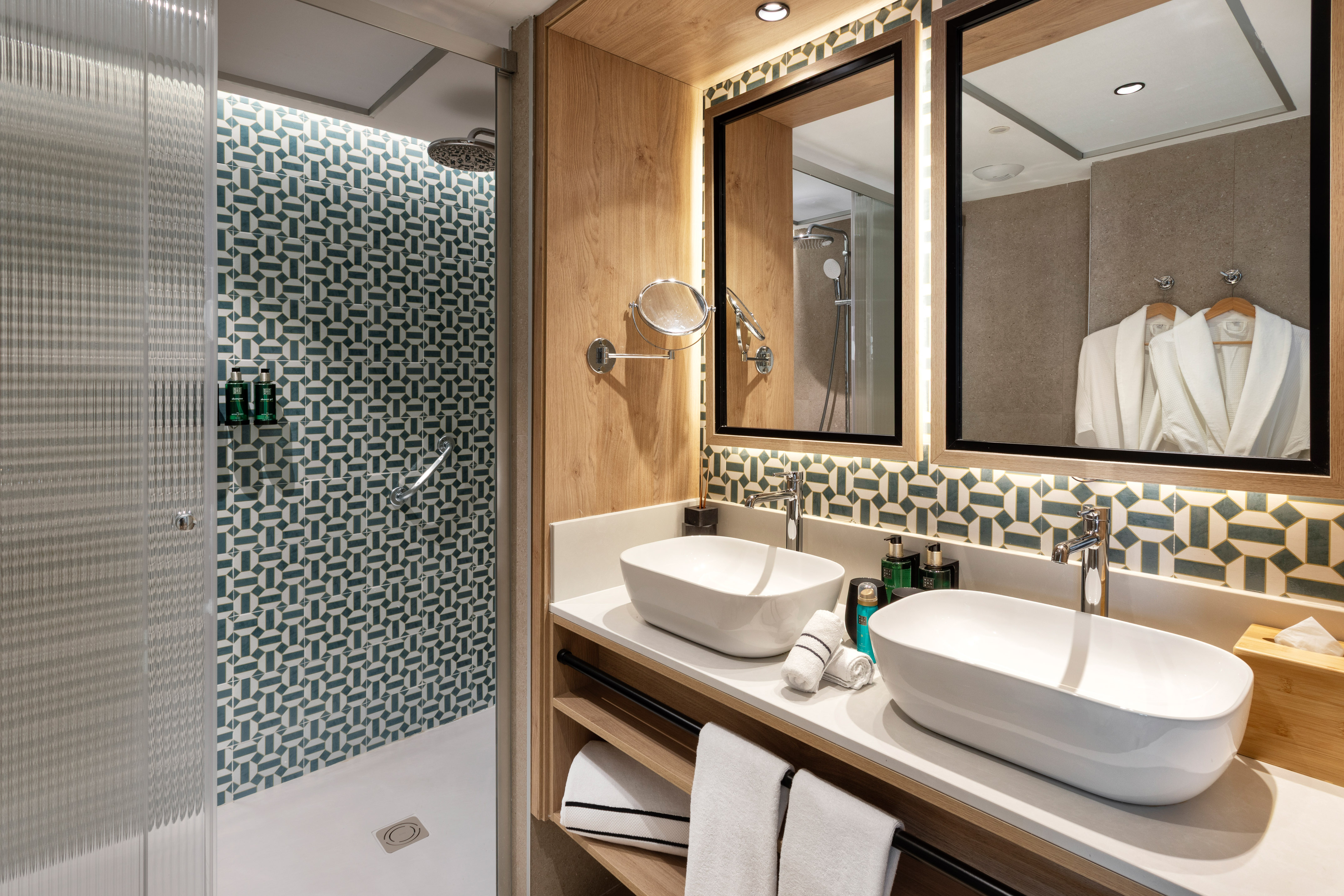 Modern bathroom with teal geometric tiled shower, dual vessel sinks, and wood vanity.
