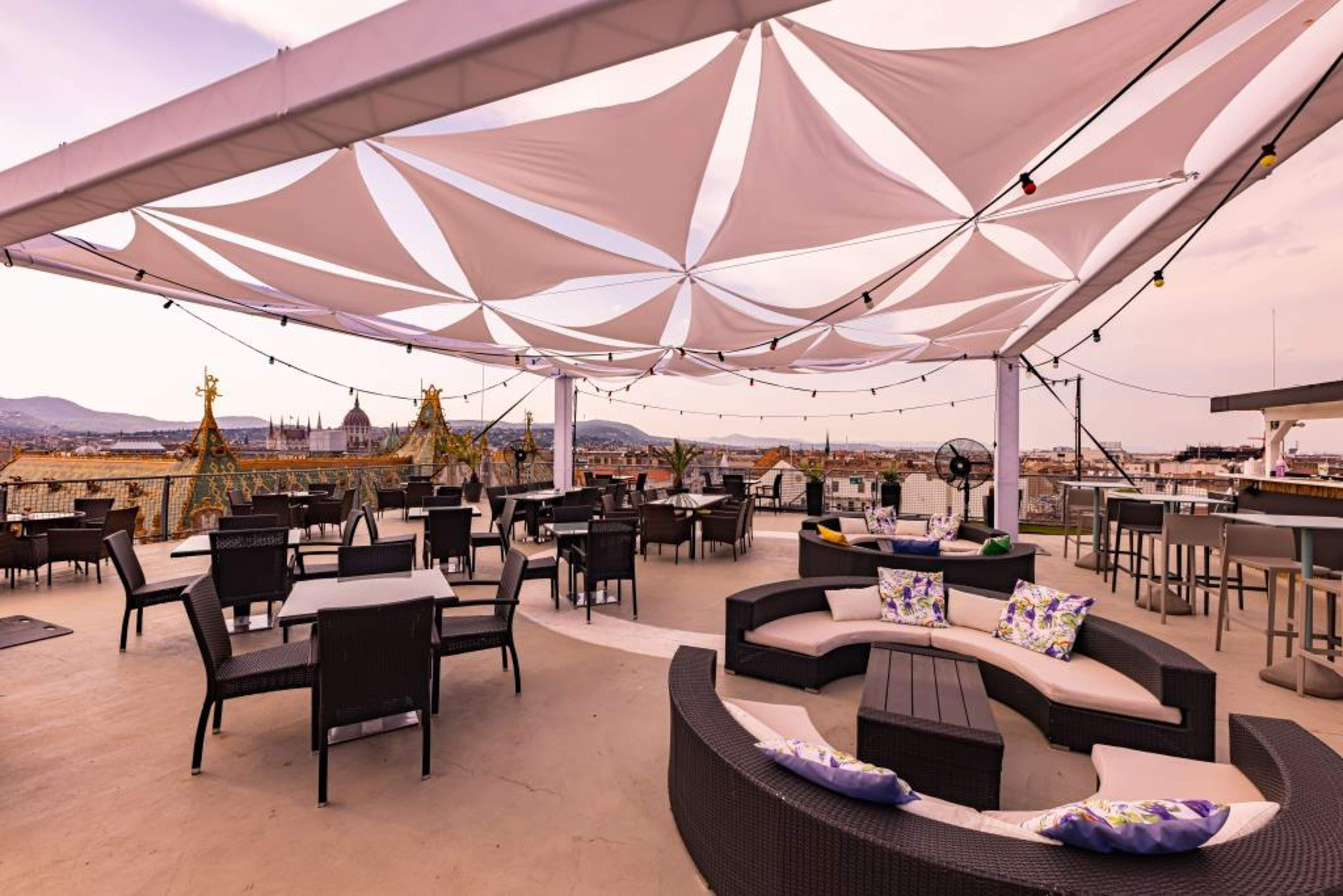 Rooftop terrace with lounge seating, tables, canopy, and Budapest skyline.