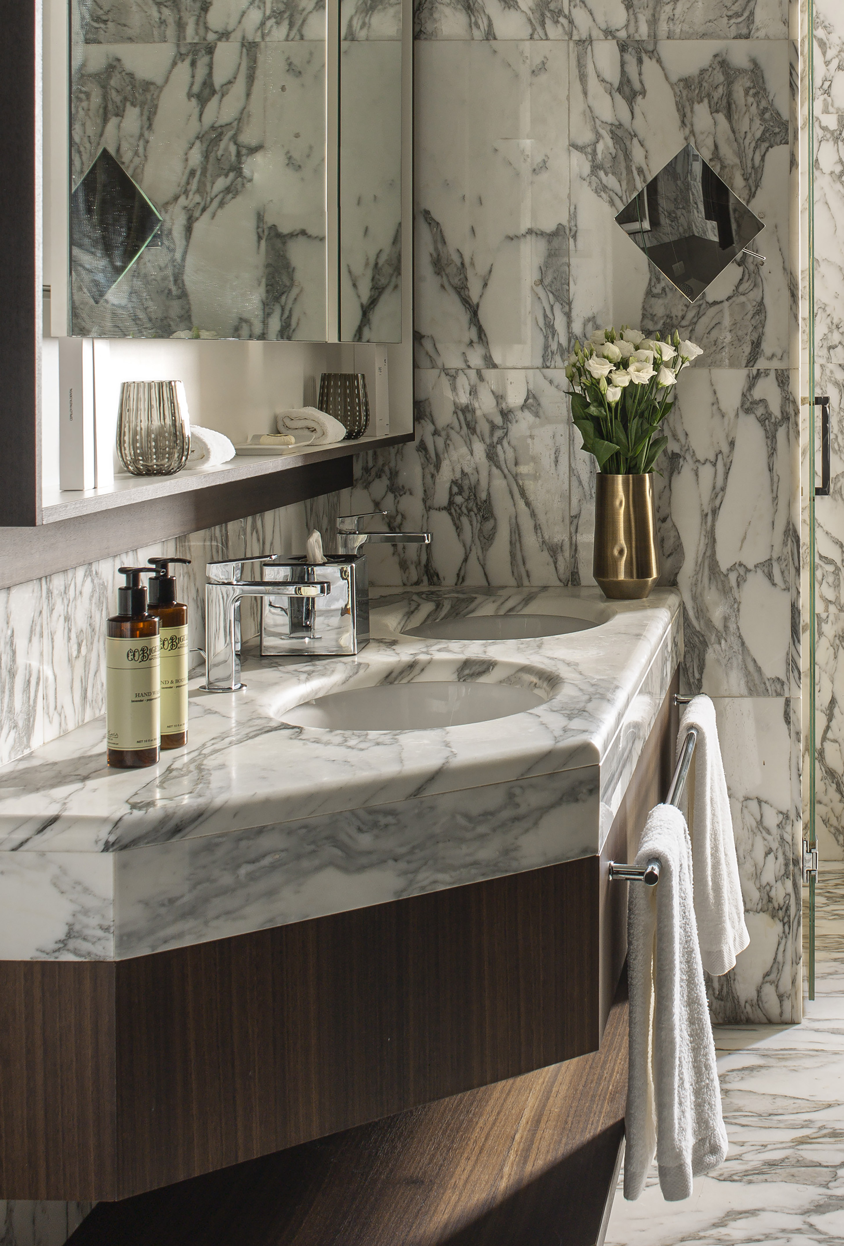 Elegant marble bathroom vanity with double sinks, wood base, and white flowers.