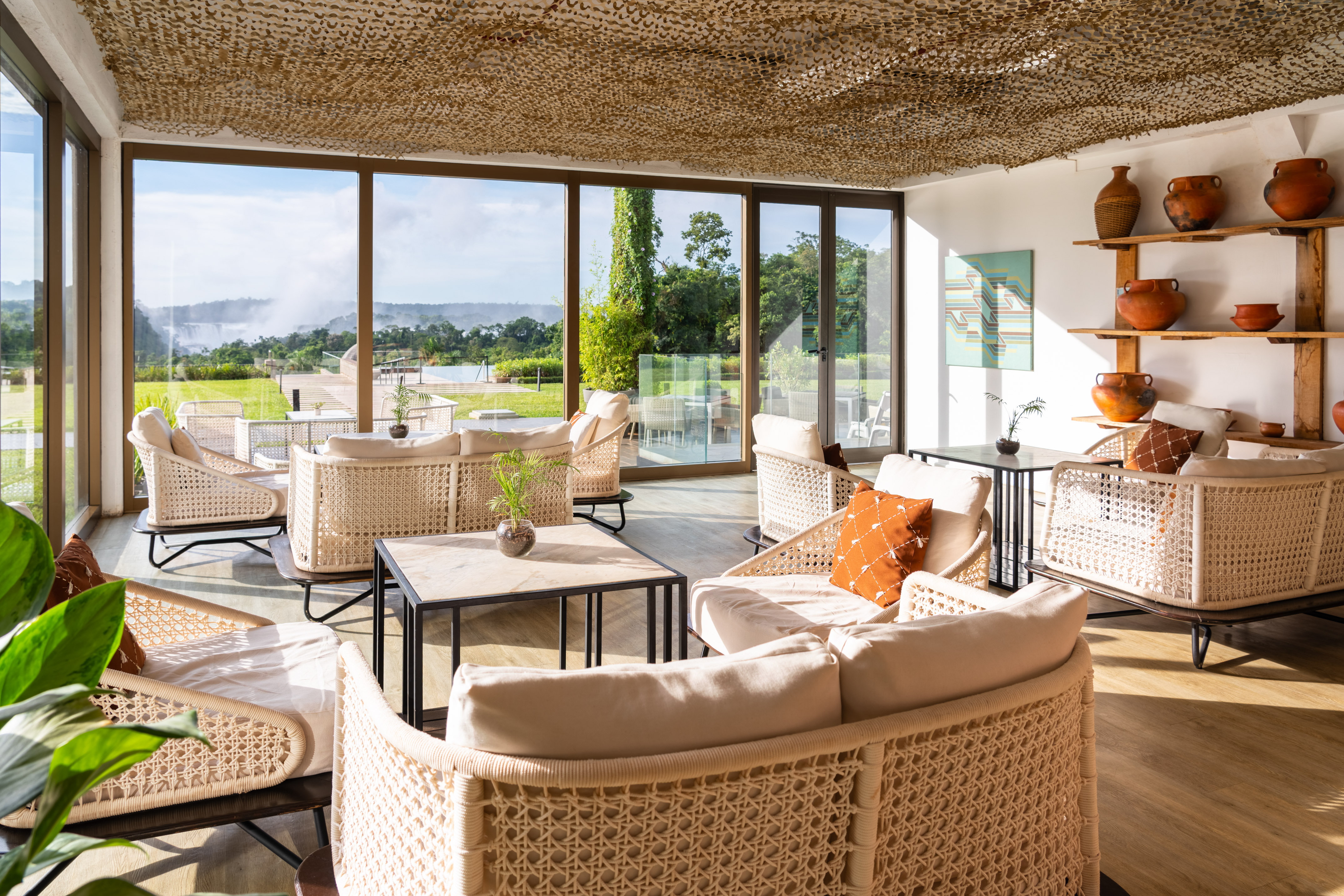 Elegant lounge with panoramic waterfall view, wicker furniture, and warm decor.