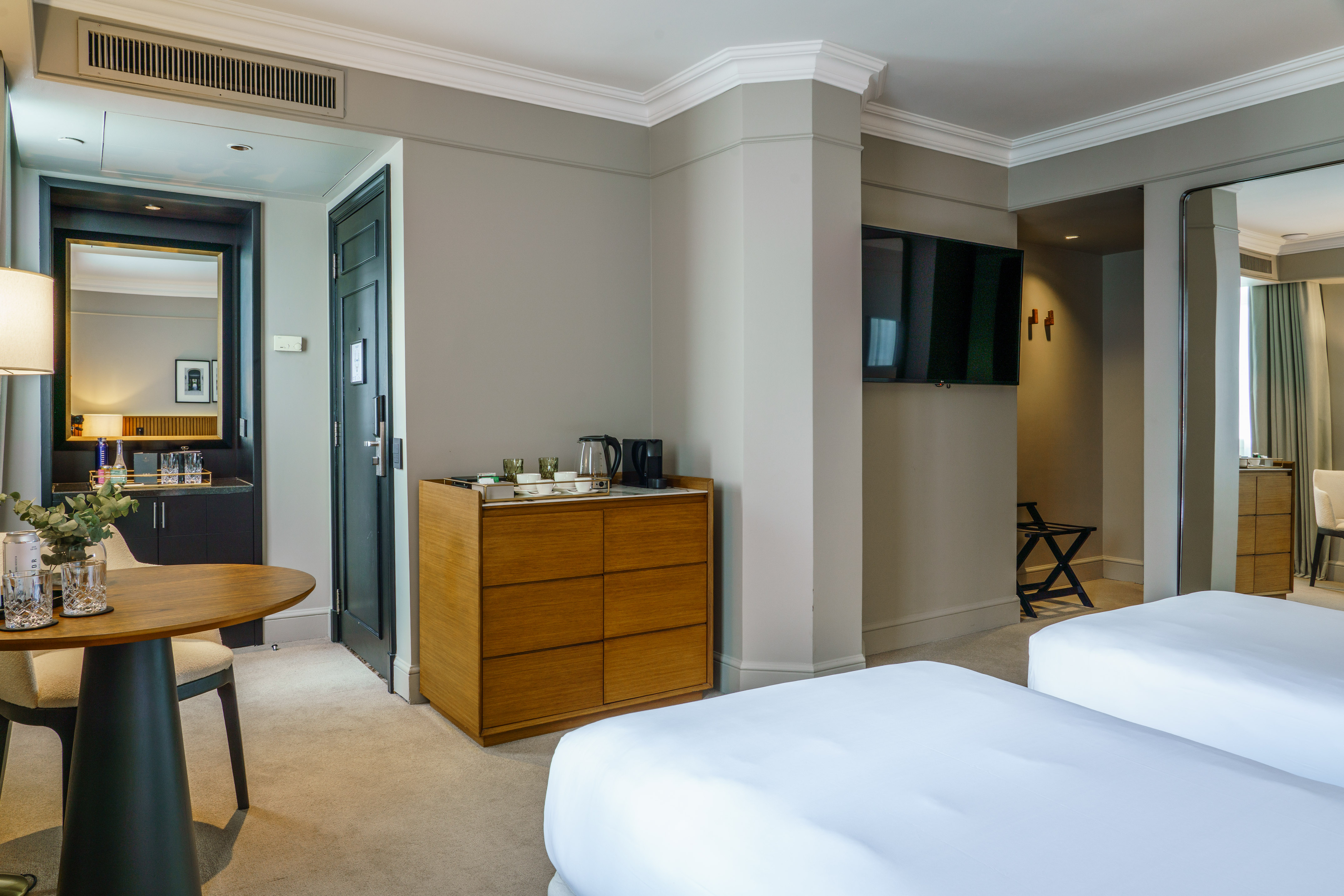 Modern hotel room with two beds, round table, coffee station, and TV.