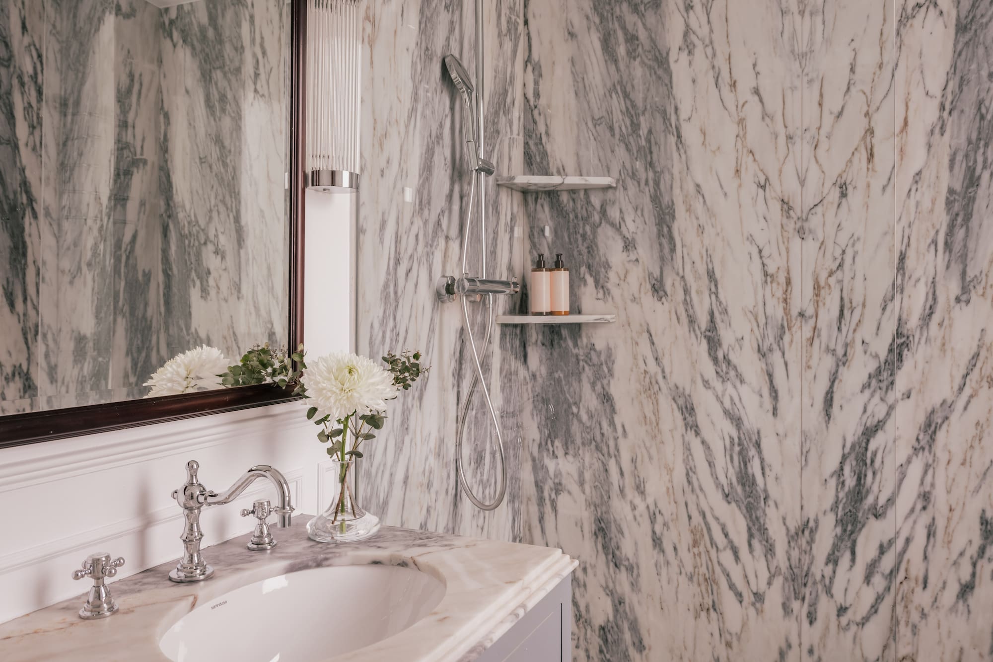 Elegant marble bathroom featuring a vanity, chrome fixtures, and a shower.