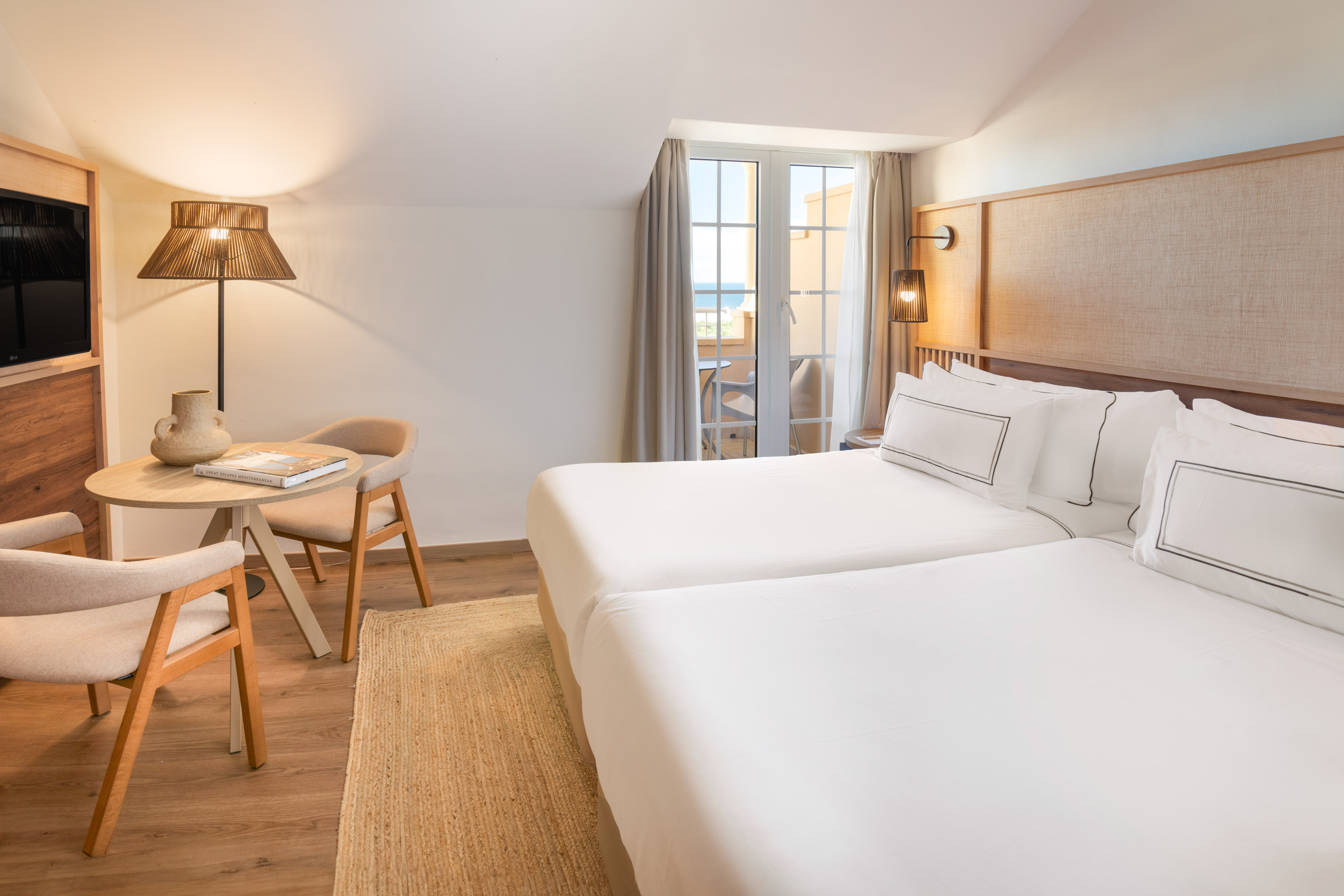 Cozy modern hotel room with twin beds, balcony sea view, and natural wood decor.