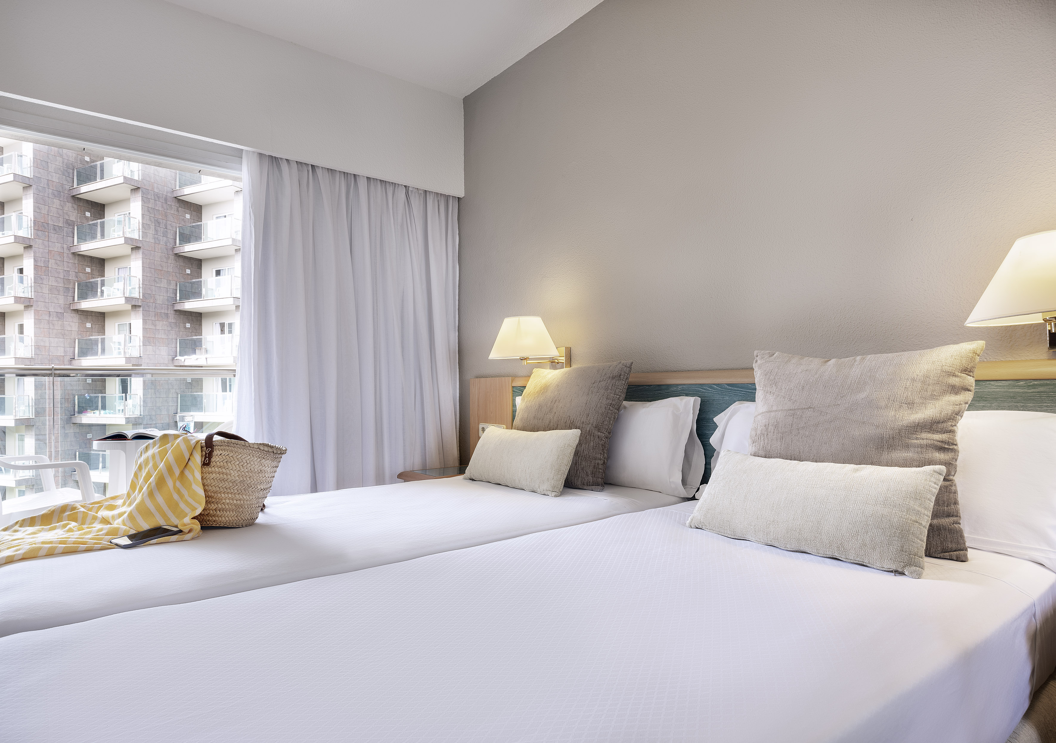 Two twin beds in a hotel room with balcony view of residential buildings.