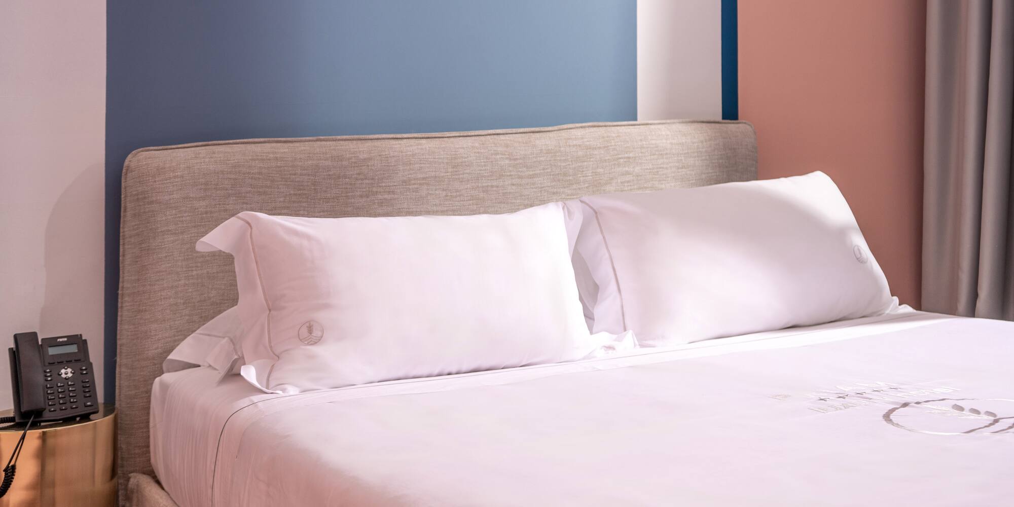 Modern hotel bed, white linen, fabric headboard, nightstand, colorful wall.