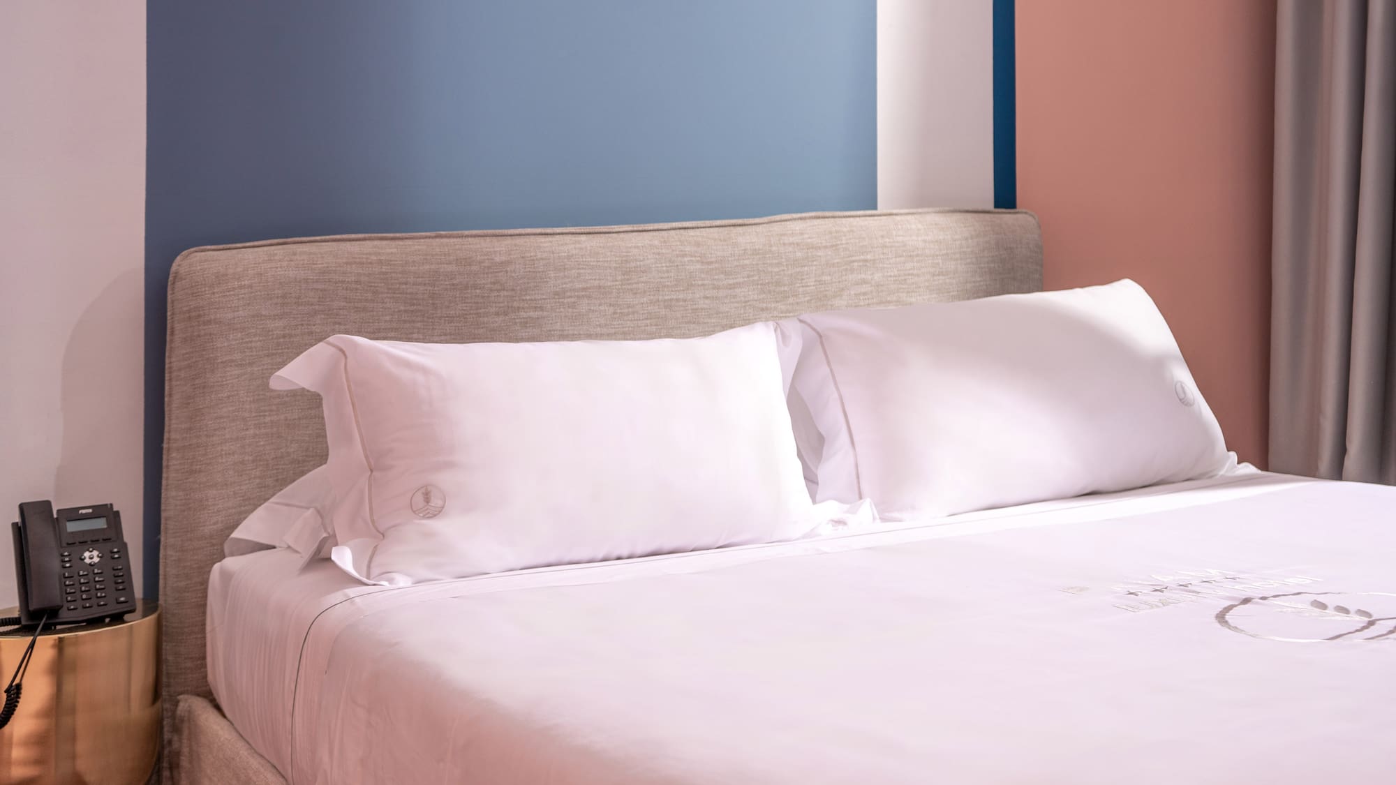 Modern hotel bed, white linen, fabric headboard, nightstand, colorful wall.