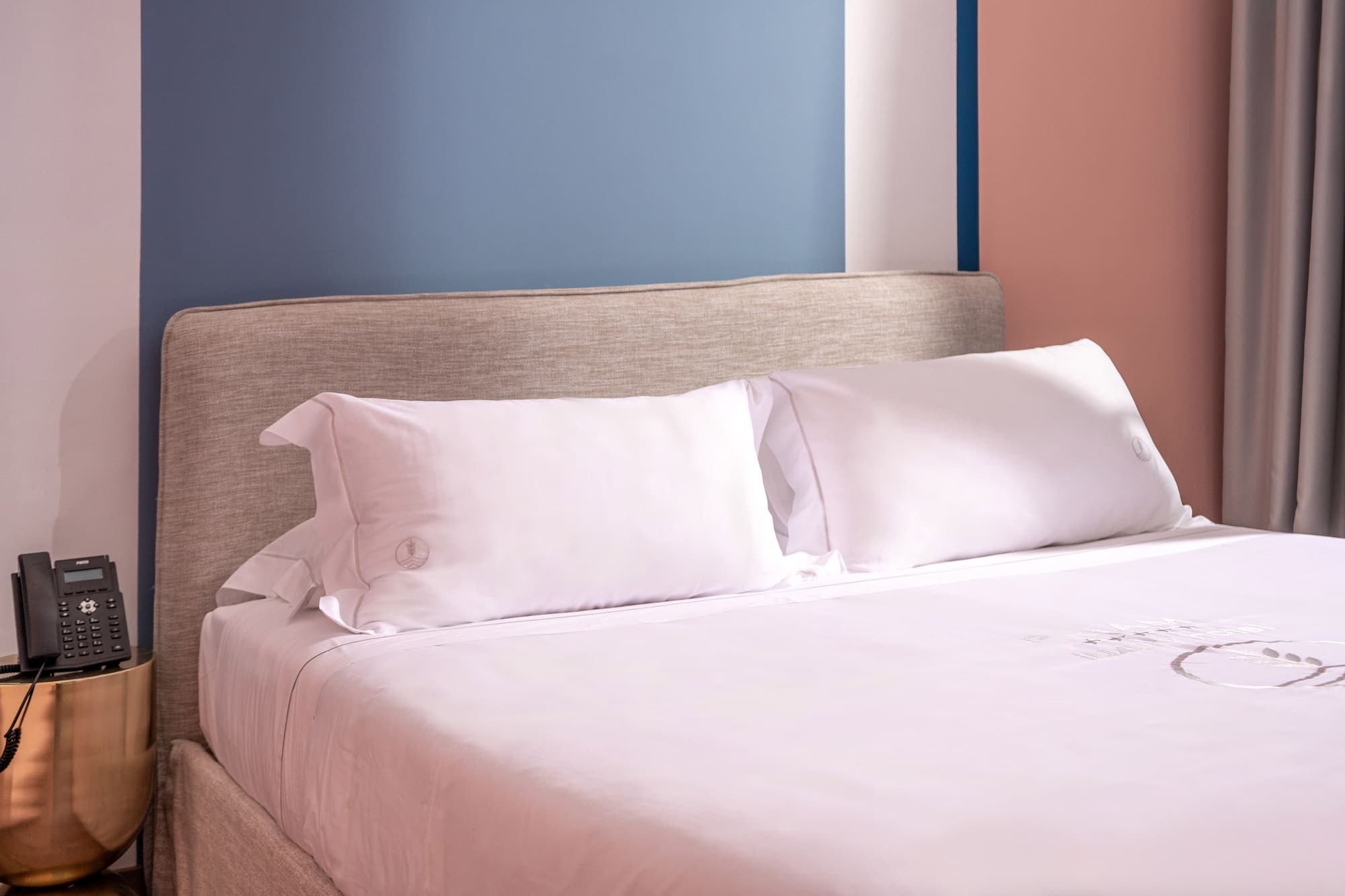 Modern hotel bed, white linen, fabric headboard, nightstand, colorful wall.