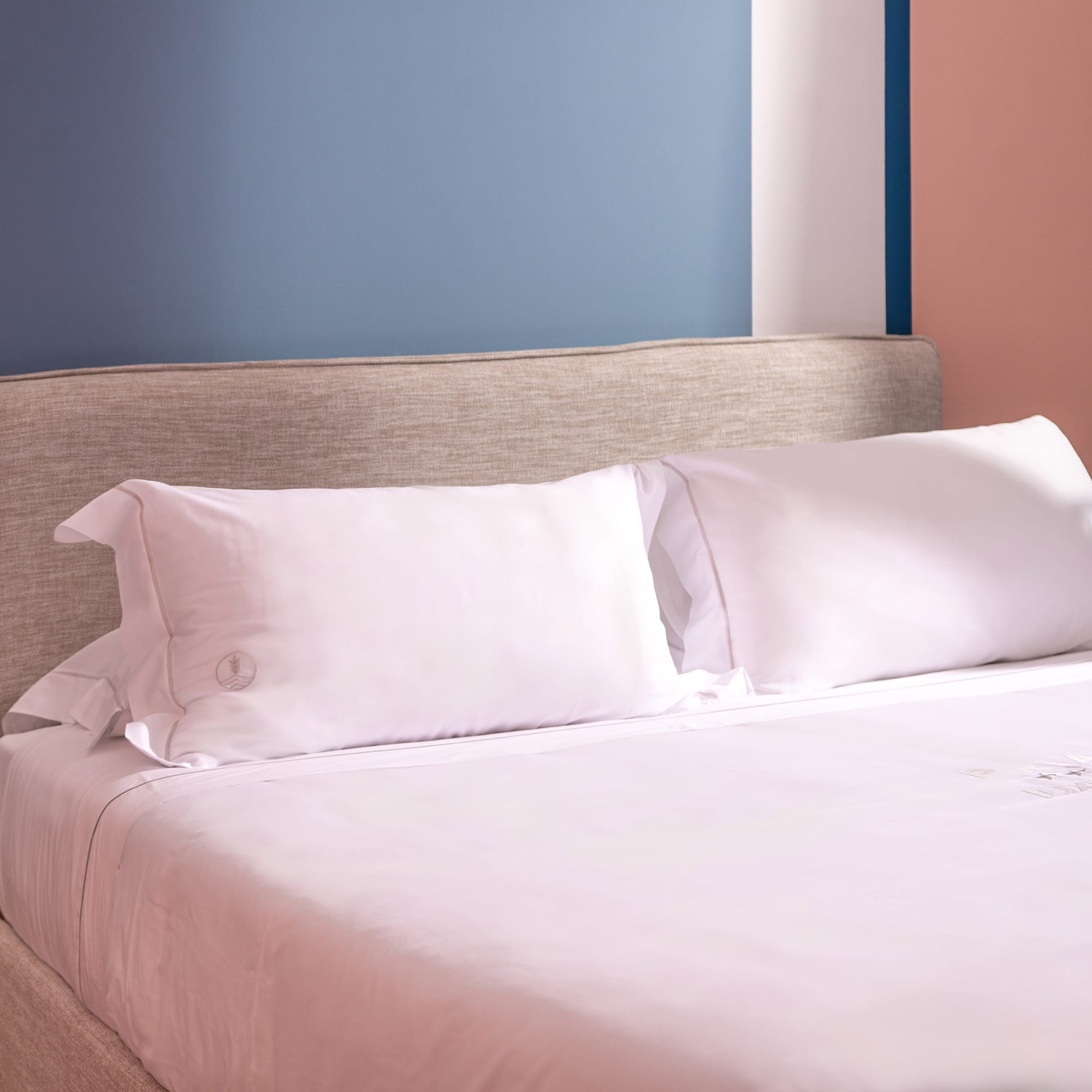 Modern hotel bed, white linen, fabric headboard, nightstand, colorful wall.