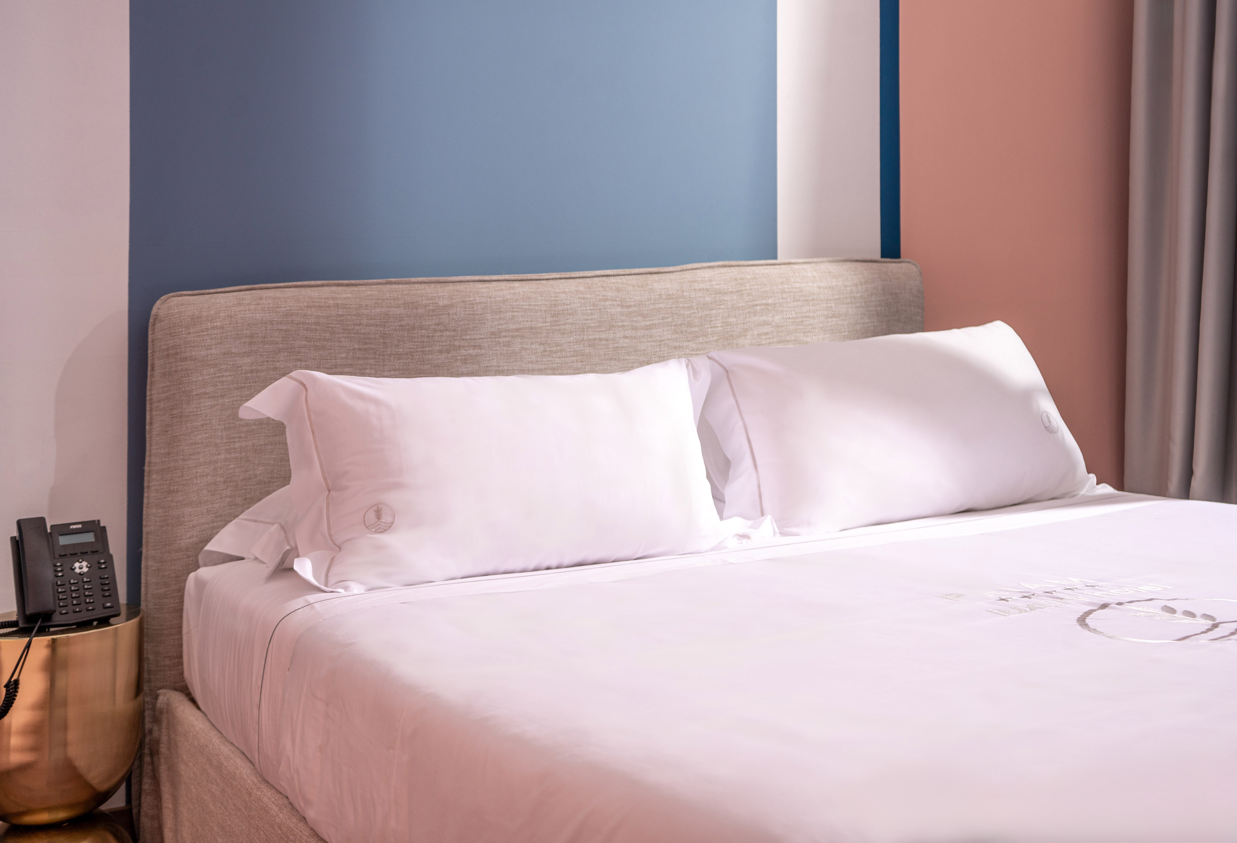 Modern hotel bed, white linen, fabric headboard, nightstand, colorful wall.