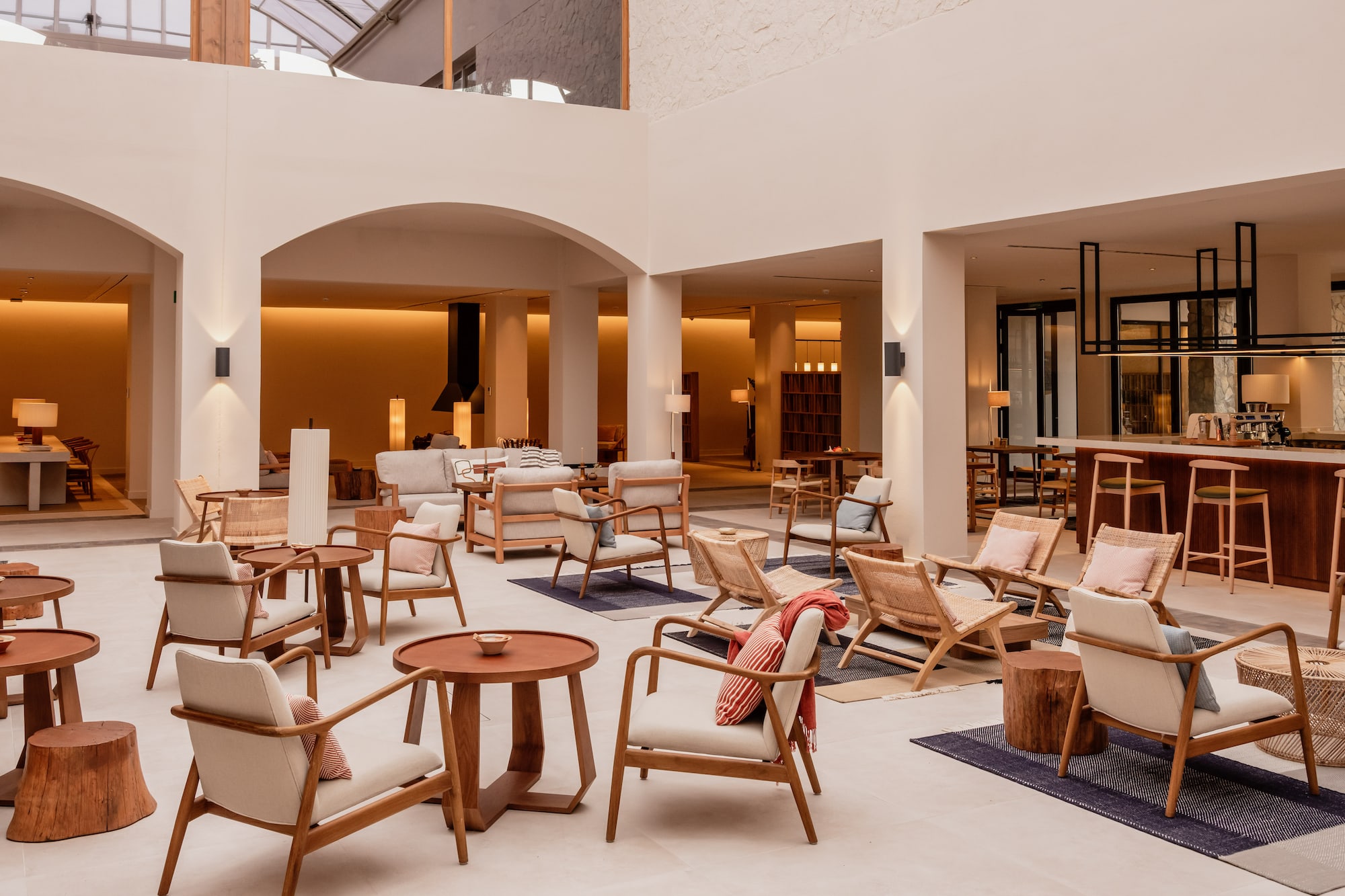 Modern hotel lobby lounge with wood armchairs, accent tables, and a bar.