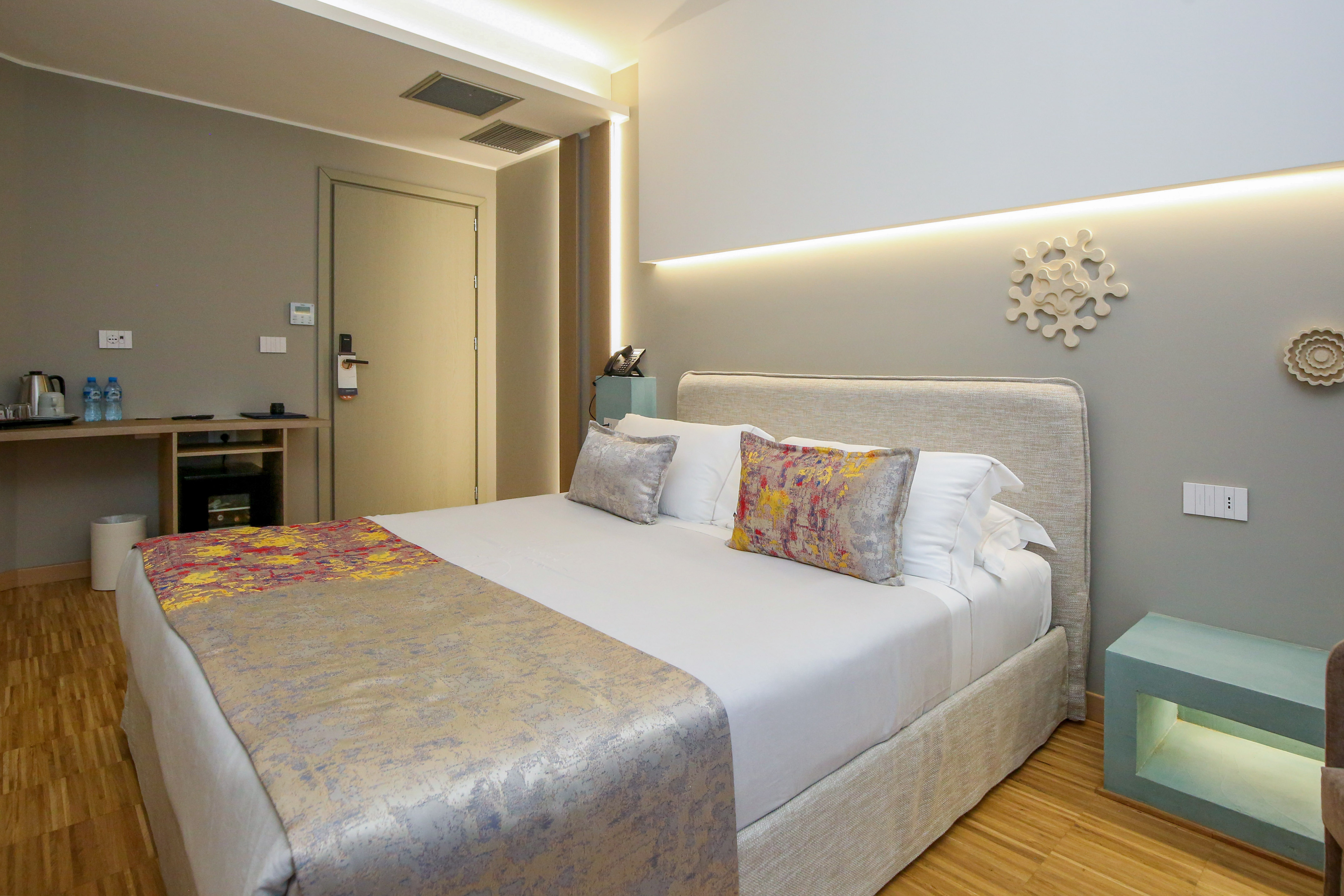 Modern hotel bedroom with abstract bedding, wood floor, and ambient lighting.