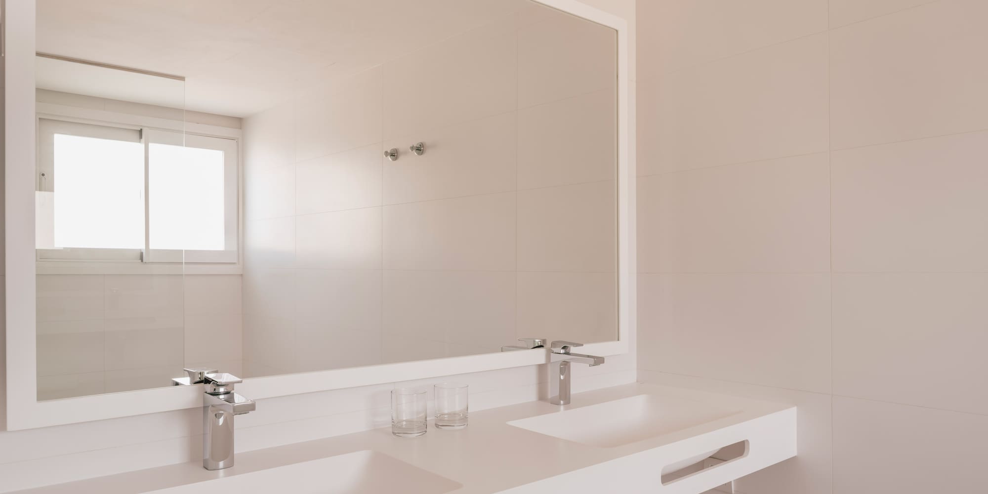 Minimalist white bathroom with double sink vanity, large mirror, and tiled walls.