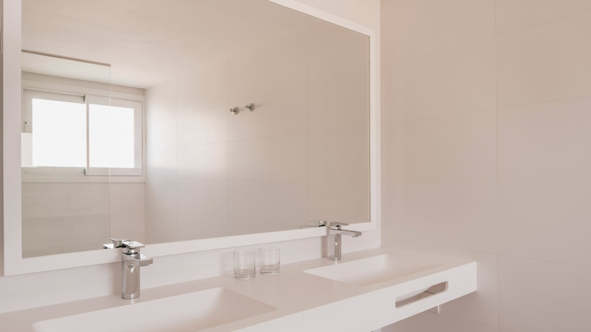 Minimalist white bathroom with double sink vanity, large mirror, and tiled walls.