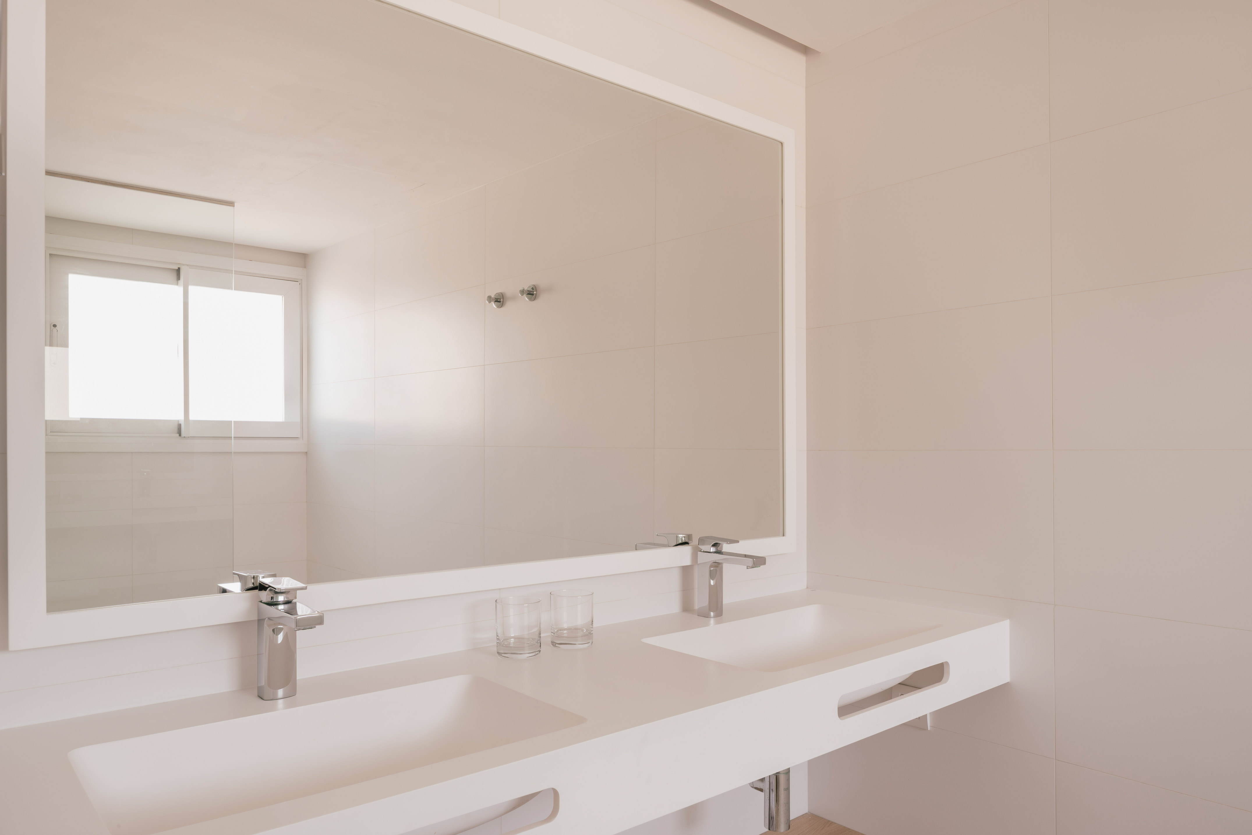 Baño moderno con doble lavabo blanco, grifos cromados y espejo rectangular.