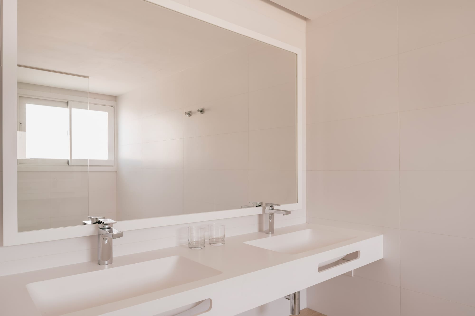 Baño moderno con doble lavabo blanco, grifos cromados y espejo rectangular.