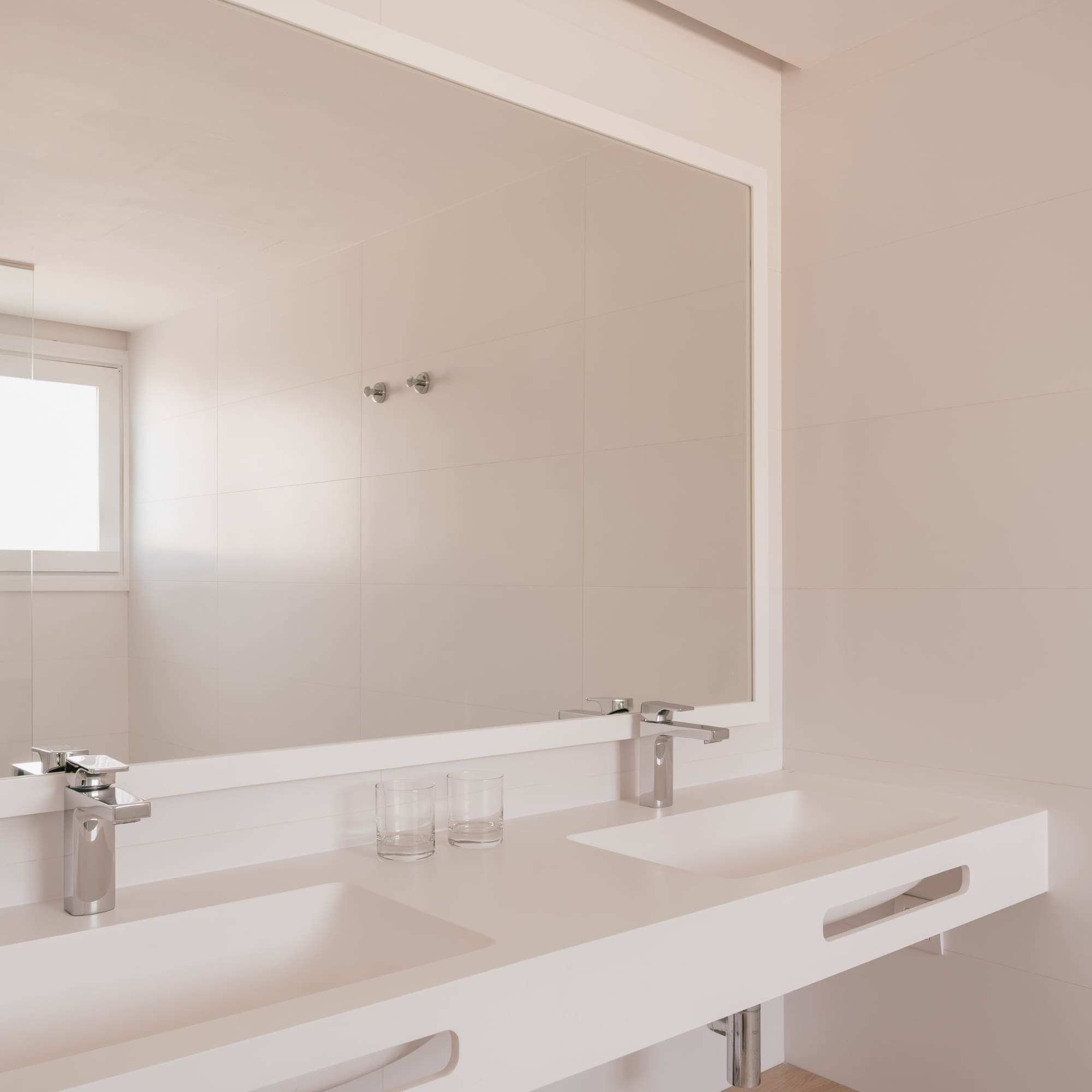 Minimalist white bathroom with double sink vanity, large mirror, and tiled walls.