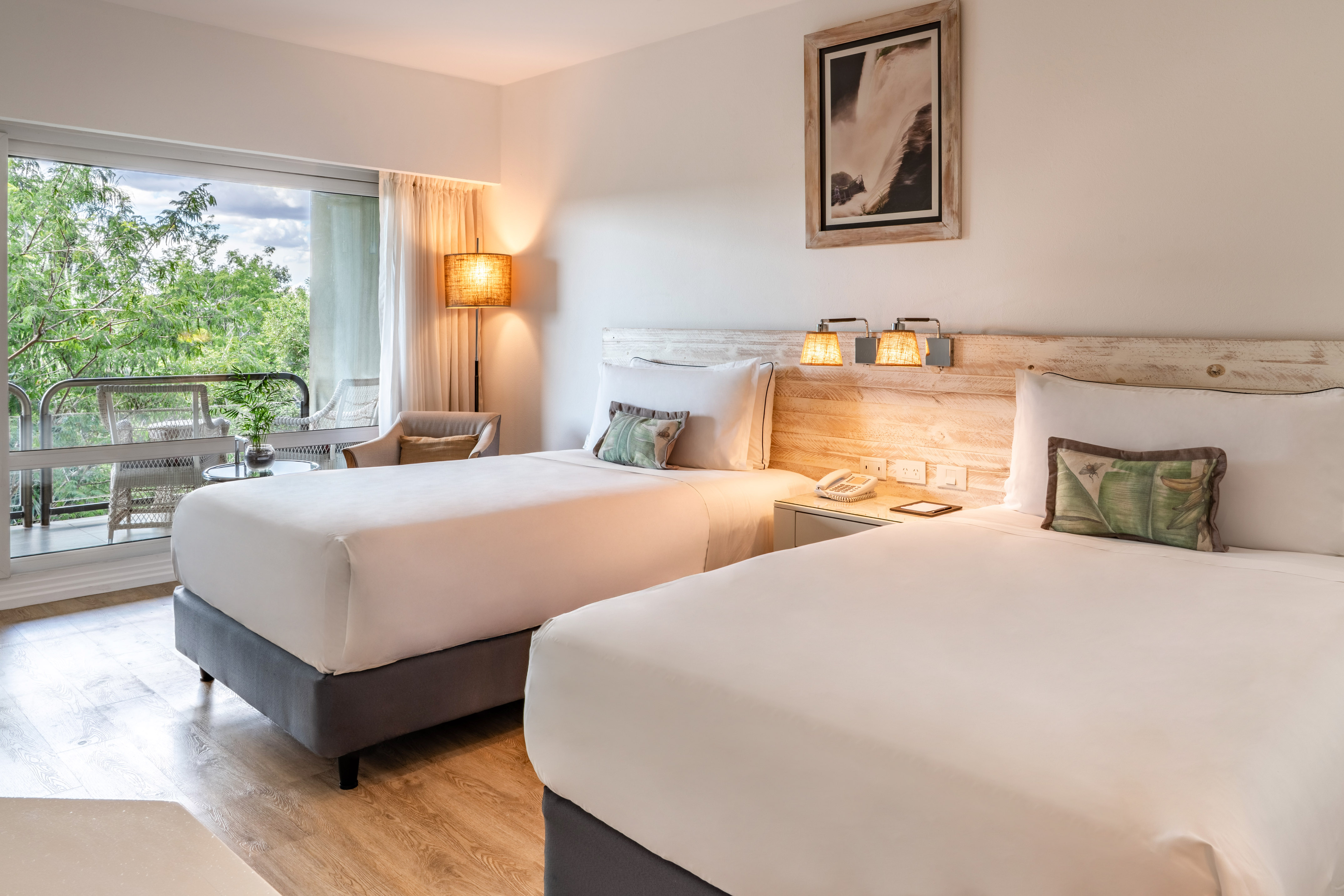 Comfortable hotel room with two twin beds, balcony, and lush nature view.
