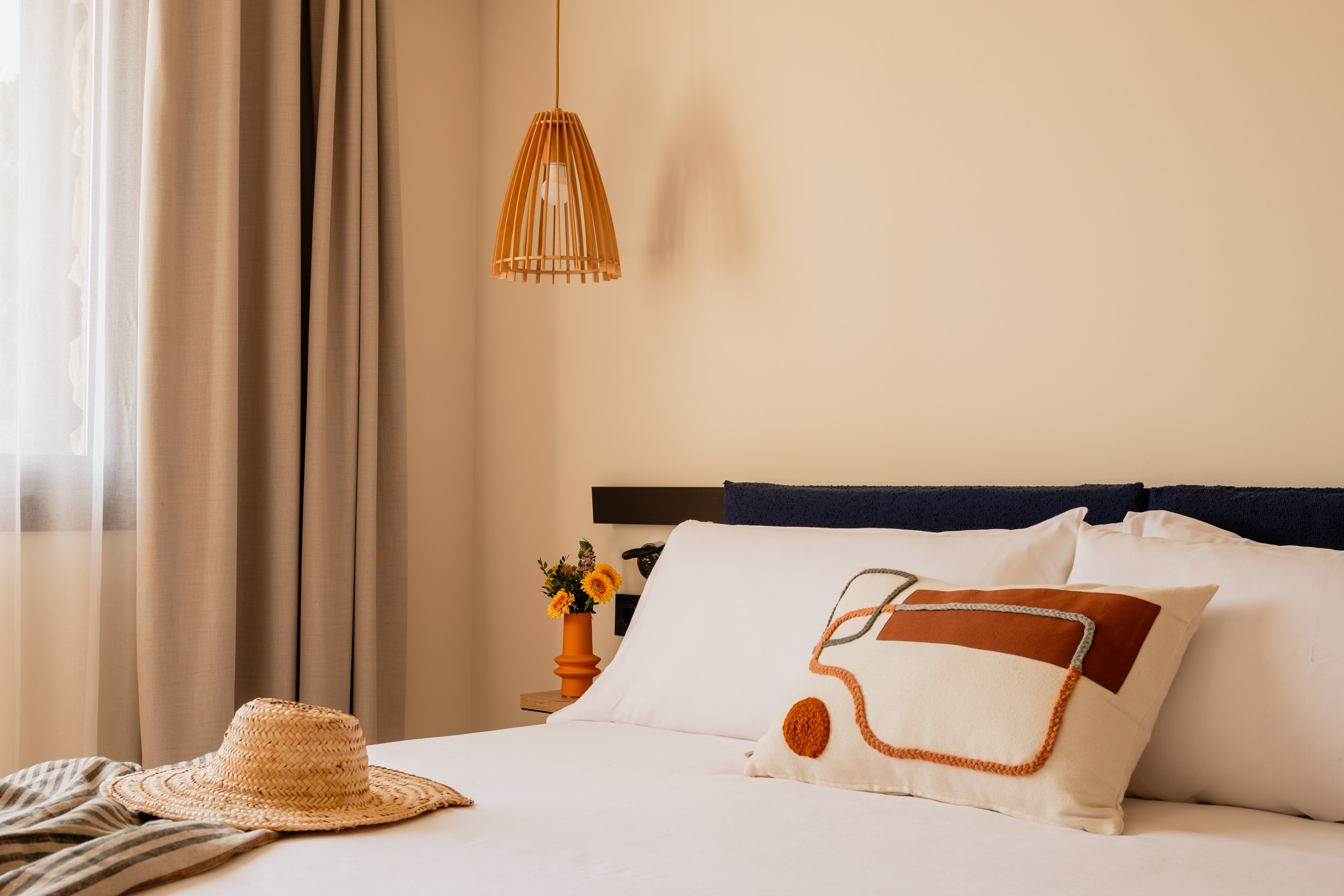 Hotel bedroom with modern decor, straw hat, and unique decorative pillow.