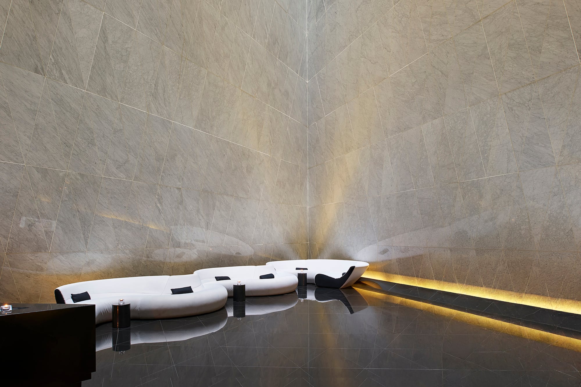 Modern lounge with grey geometric wall tiles, black polished floor, white sofa.