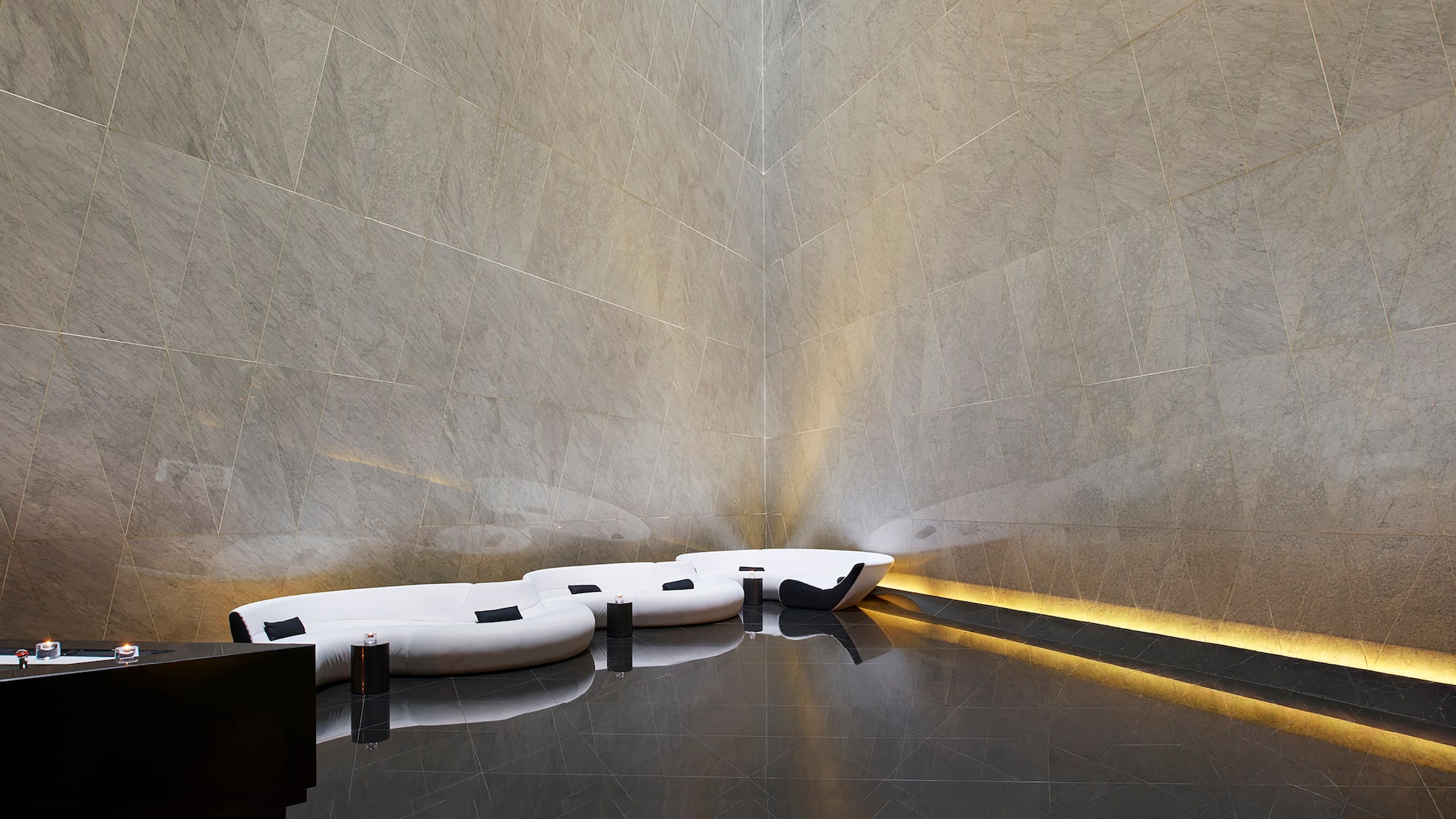 Modern lounge with grey geometric tiled walls, white sofas, and reflective floor.
