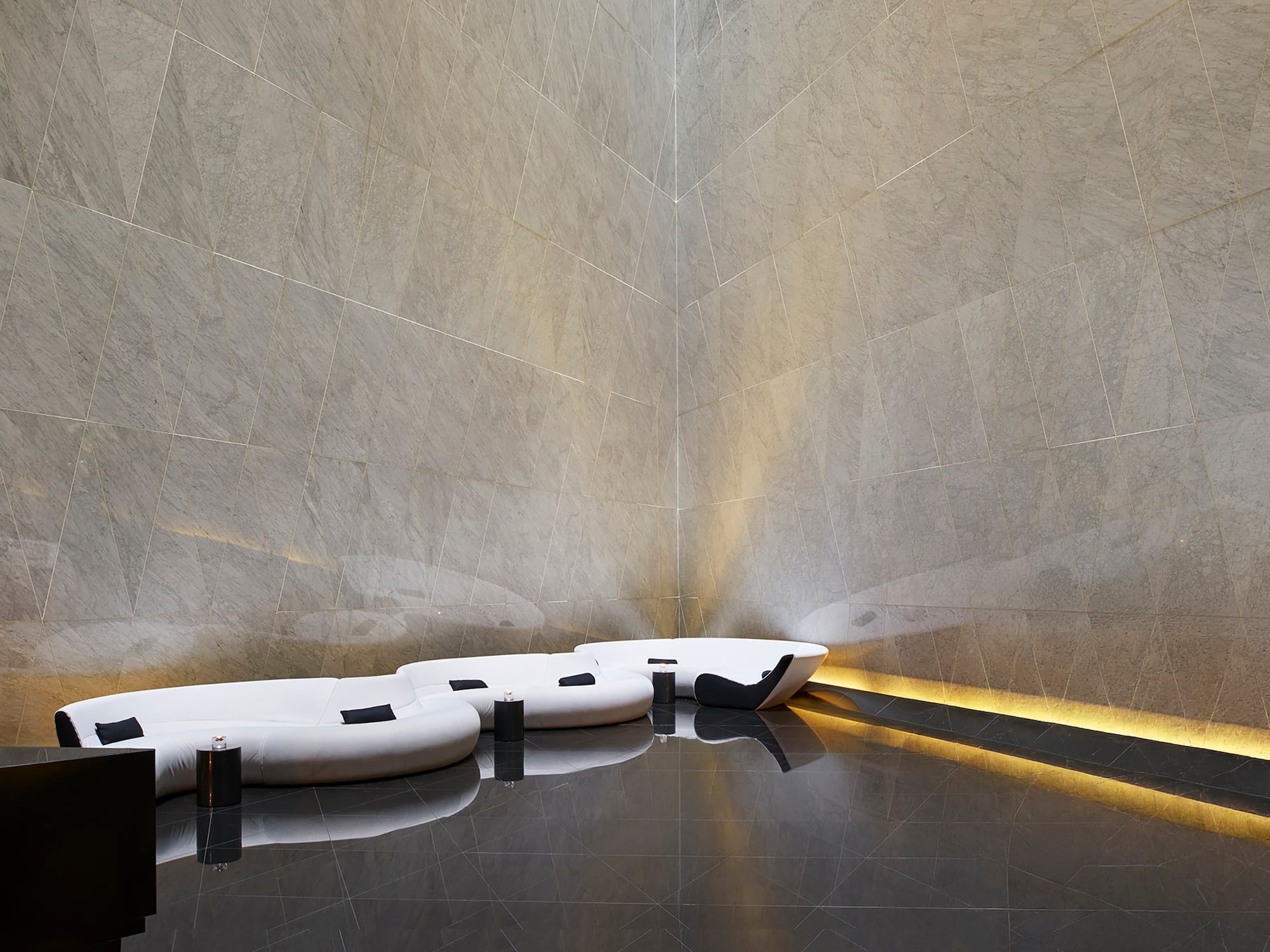 Modern lounge with grey geometric wall tiles, black polished floor, white sofa.