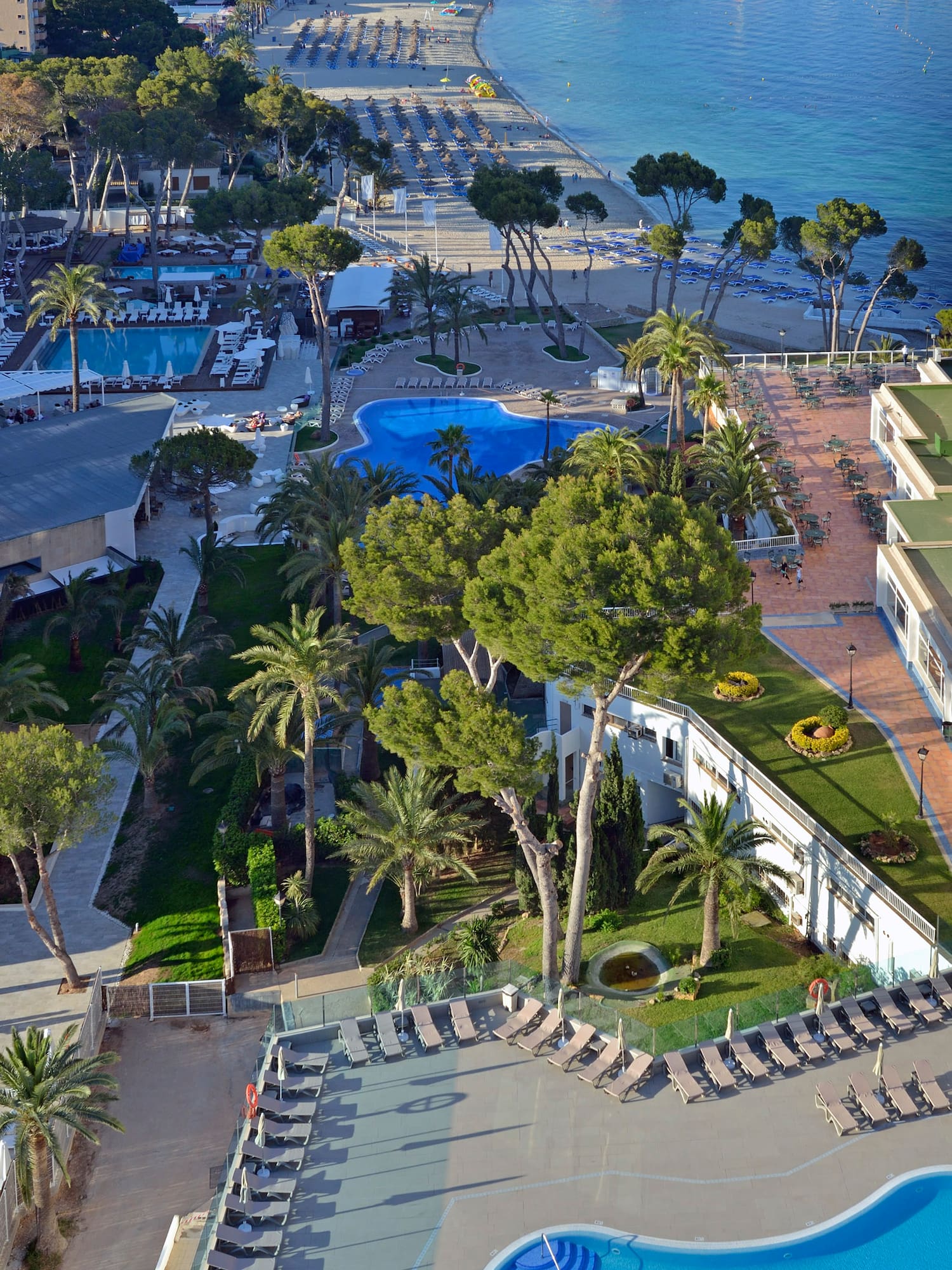 Sunny resort, multiple pools, sandy beach, blue ocean, and coastal hotels.