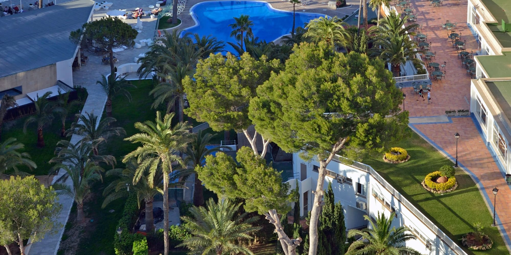 Sunny coastal resort aerial view: beach, blue pools, hotels, ocean.