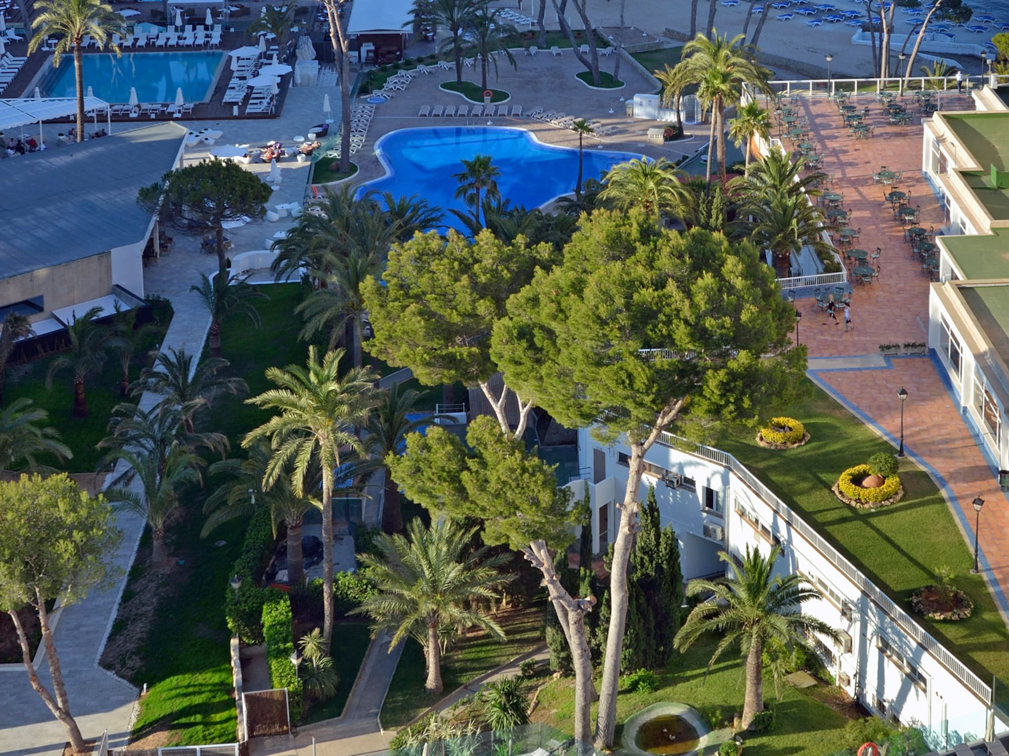 Sunny resort, multiple pools, sandy beach, blue ocean, and coastal hotels.