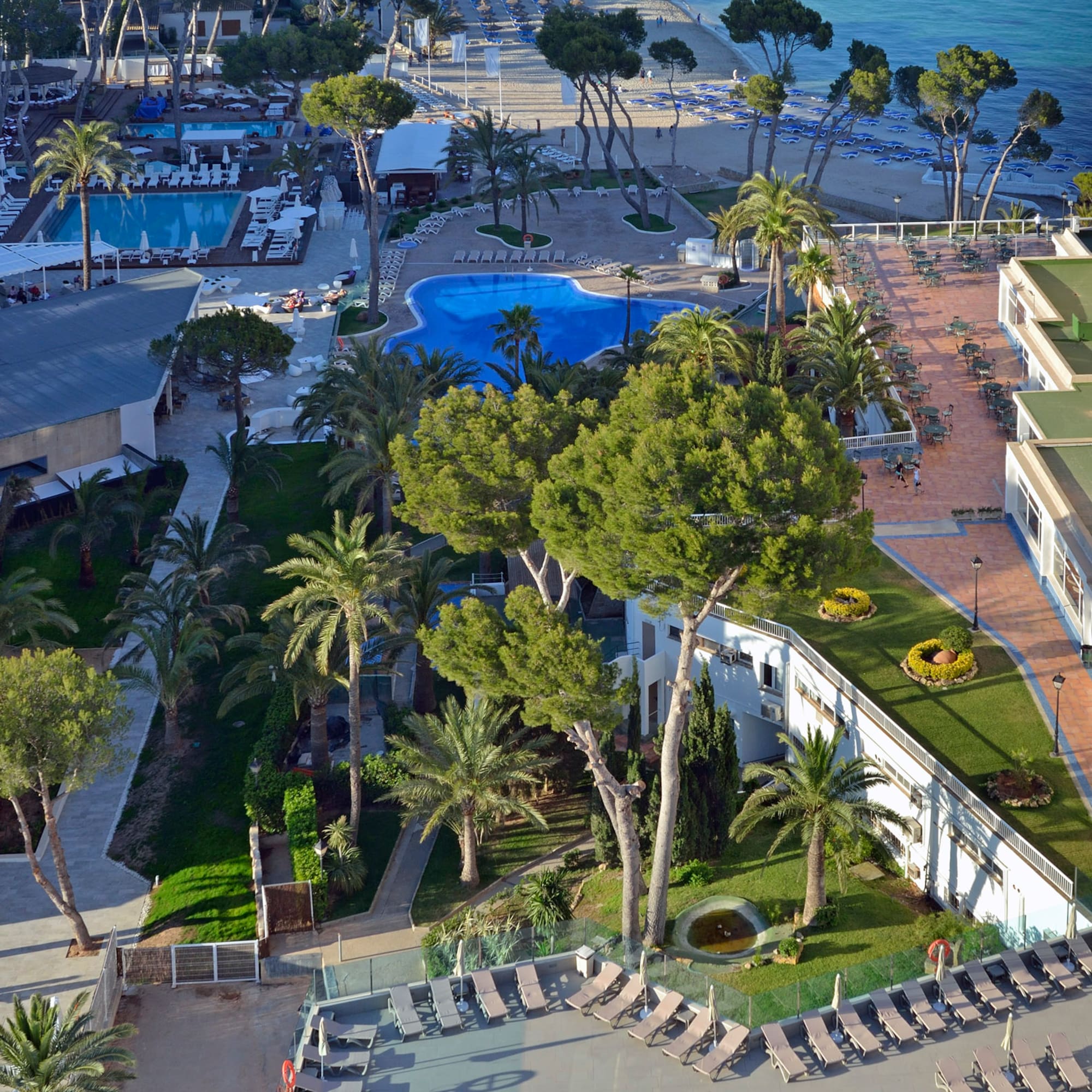 Sunny coastal resort aerial view: beach, blue pools, hotels, ocean.