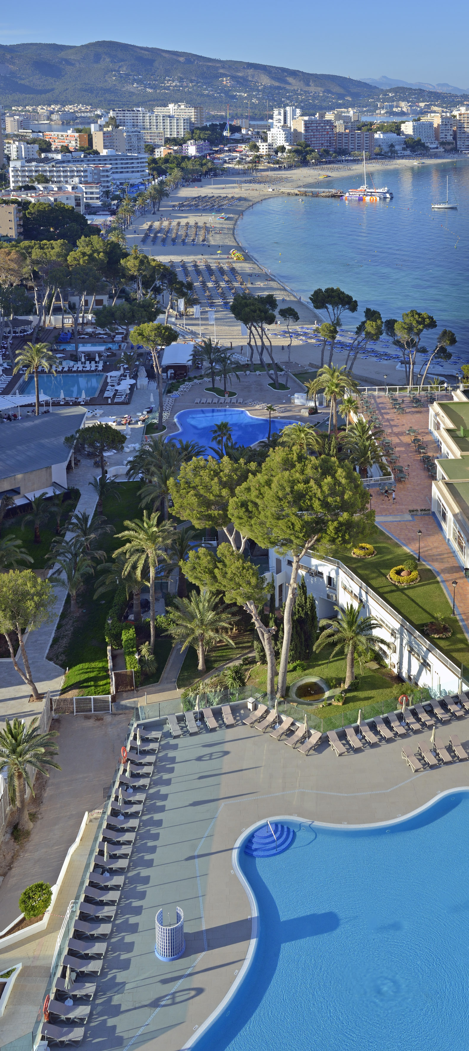 Sunny resort, multiple pools, sandy beach, blue ocean, and coastal hotels.