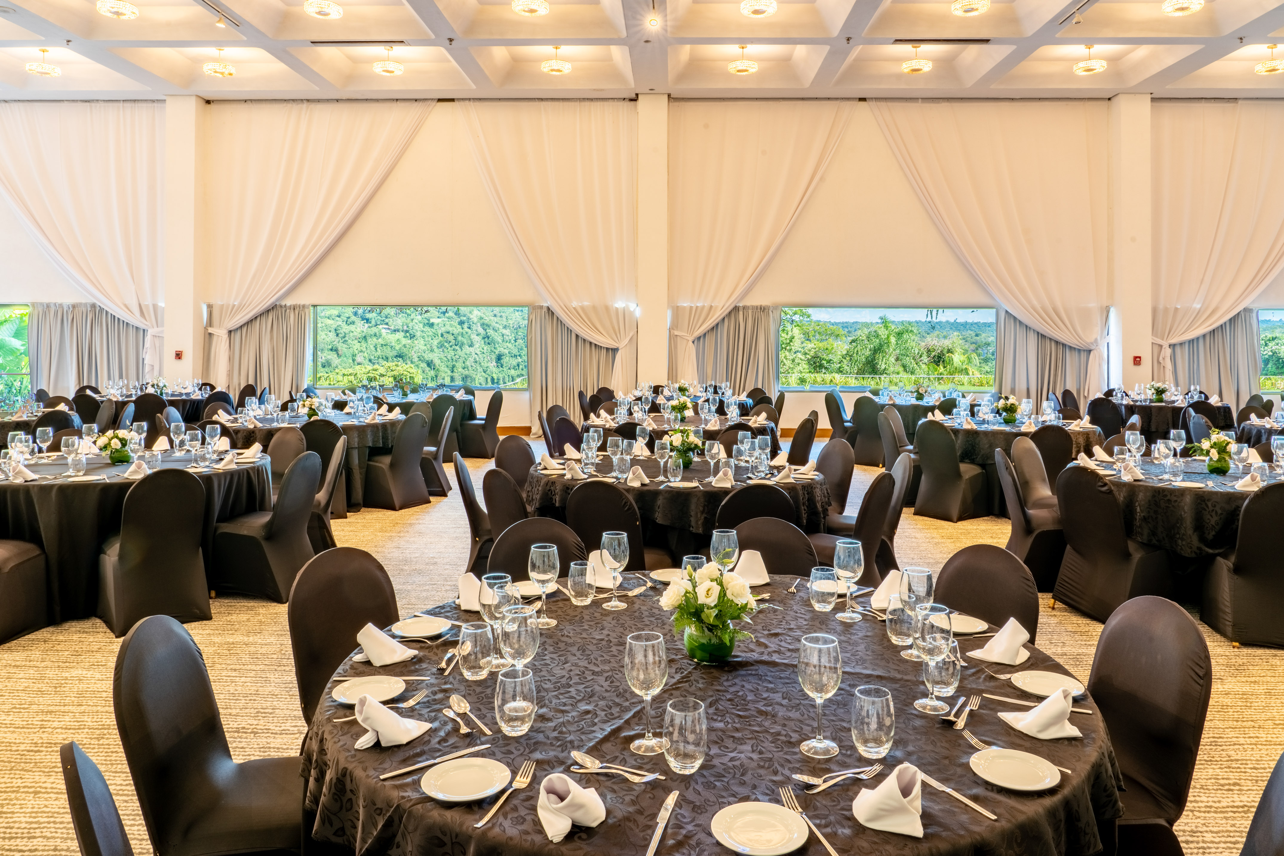 Ballroom set with black tables, formal place settings, and scenic nature views.