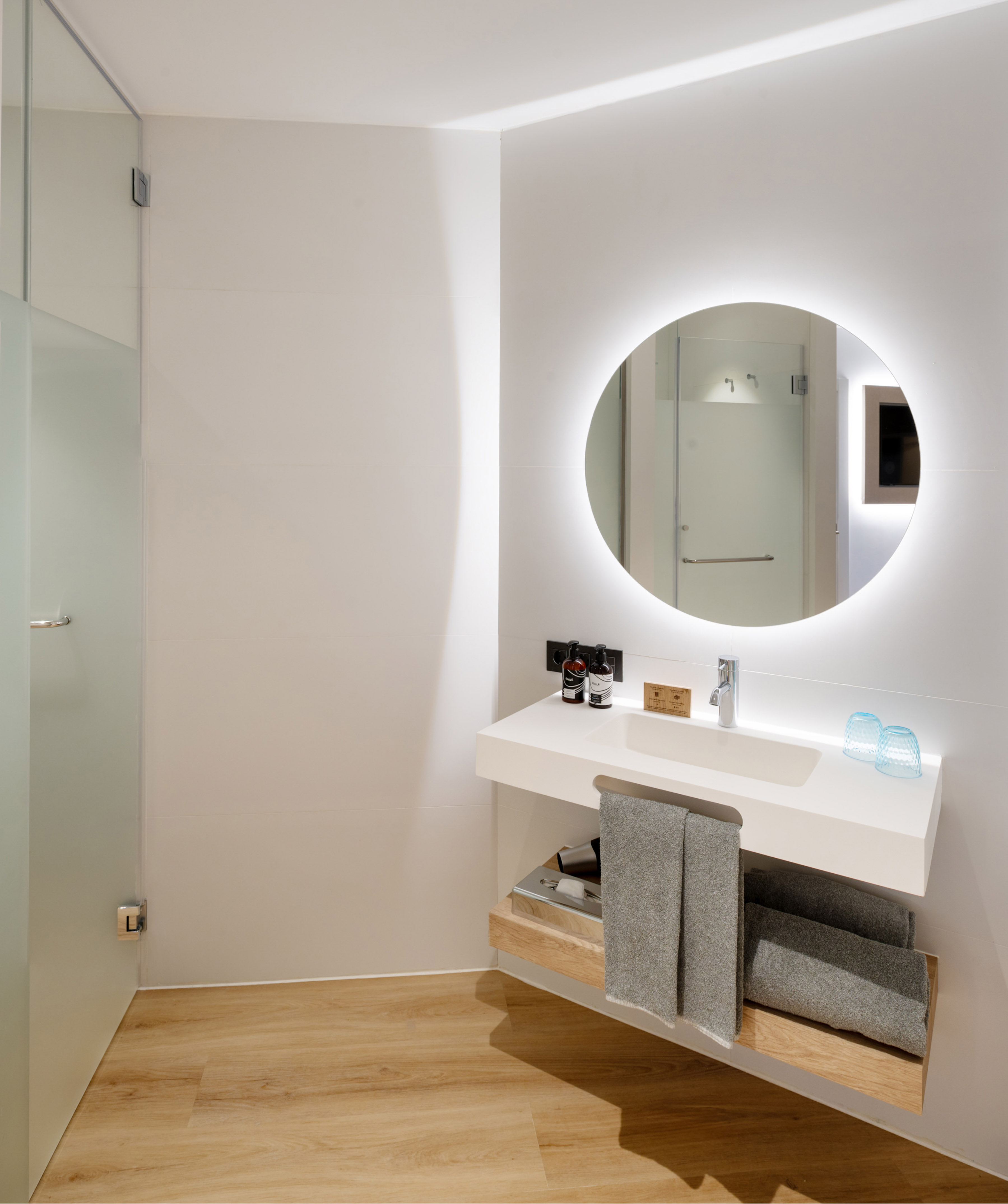 Modern bathroom with floating vanity, backlit mirror, white walls, and wood floor.