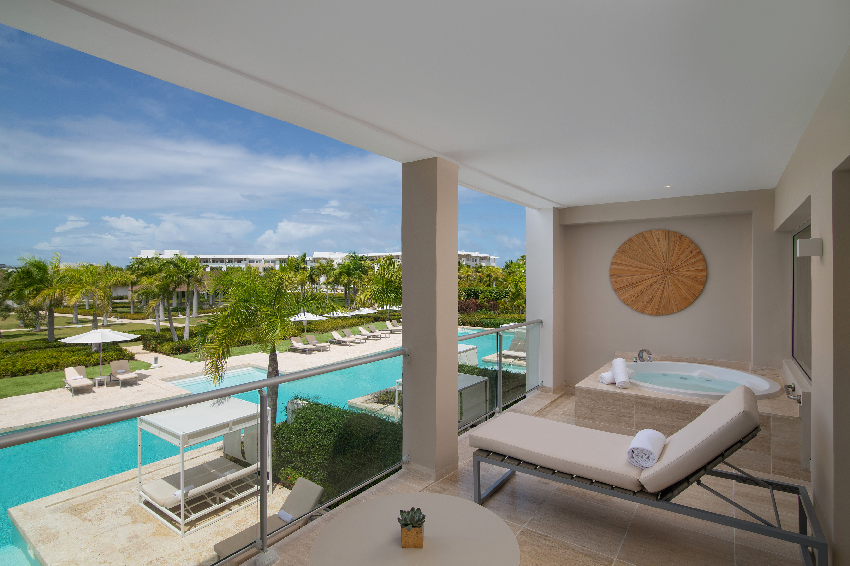 Luxury hotel balcony with outdoor jacuzzi, lounge chair, and resort pool view.