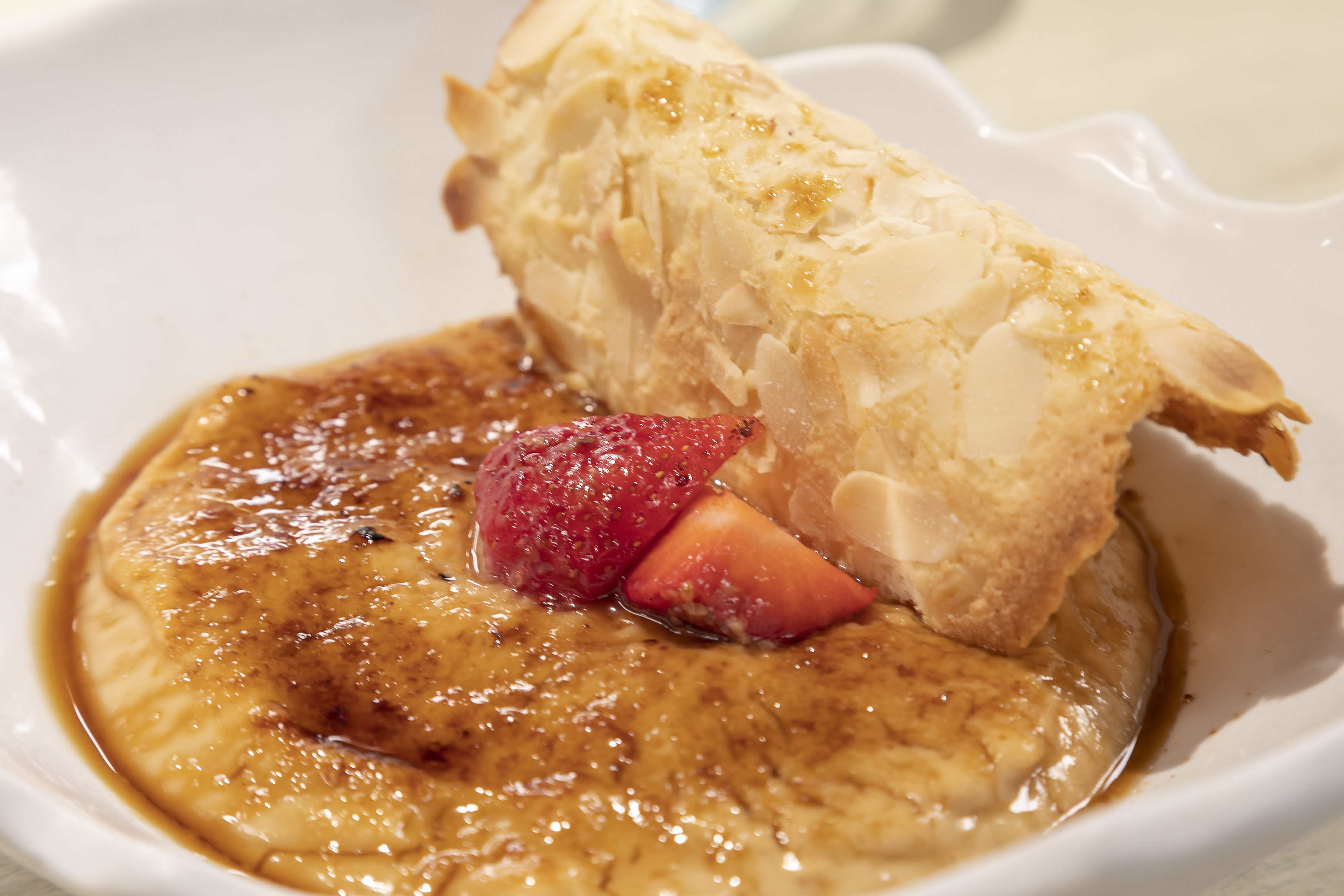 Caramelized crème brûlée dessert with fresh strawberries and almond tuile.