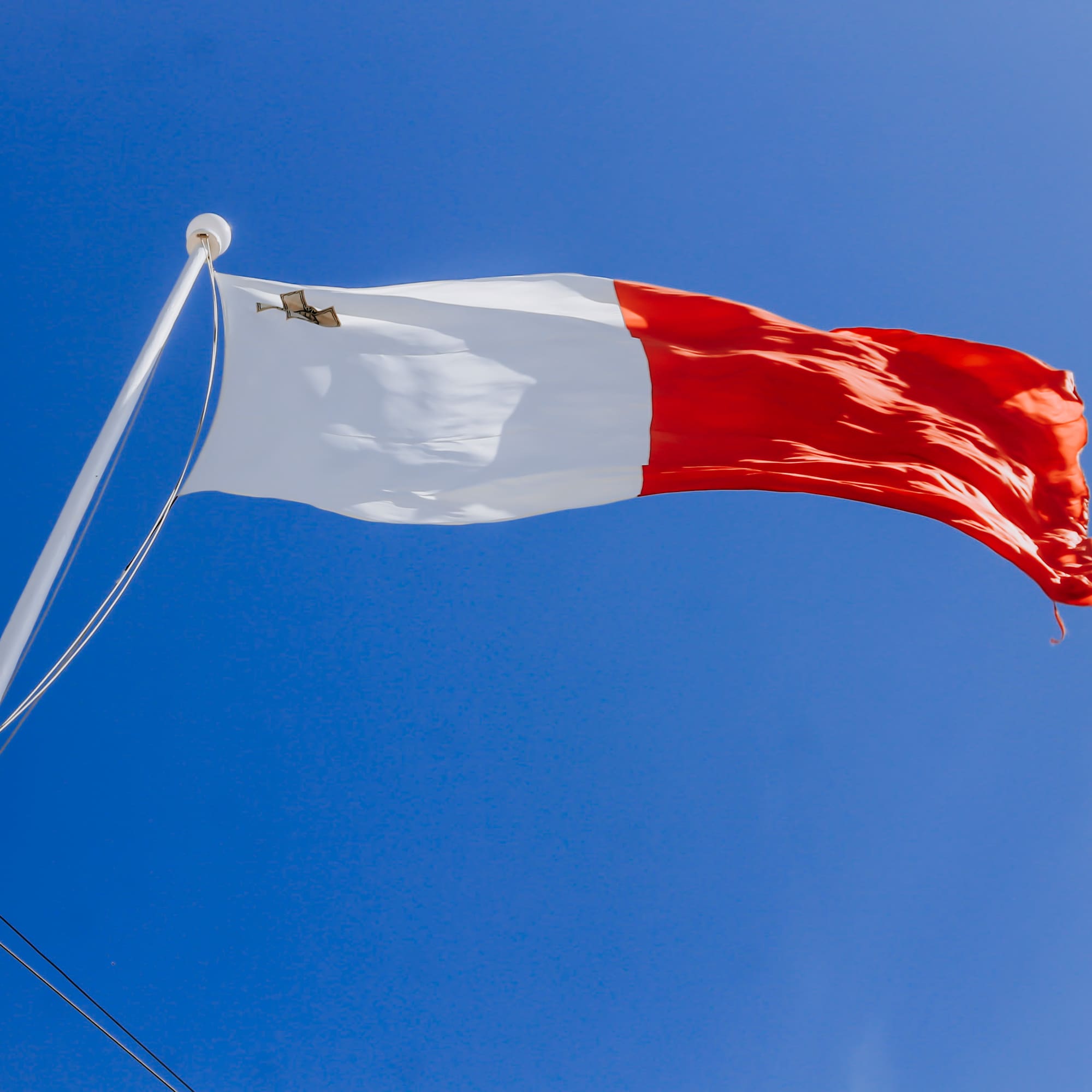 Malta flag waving against a clear blue sky, showing white, red, and George Cross.