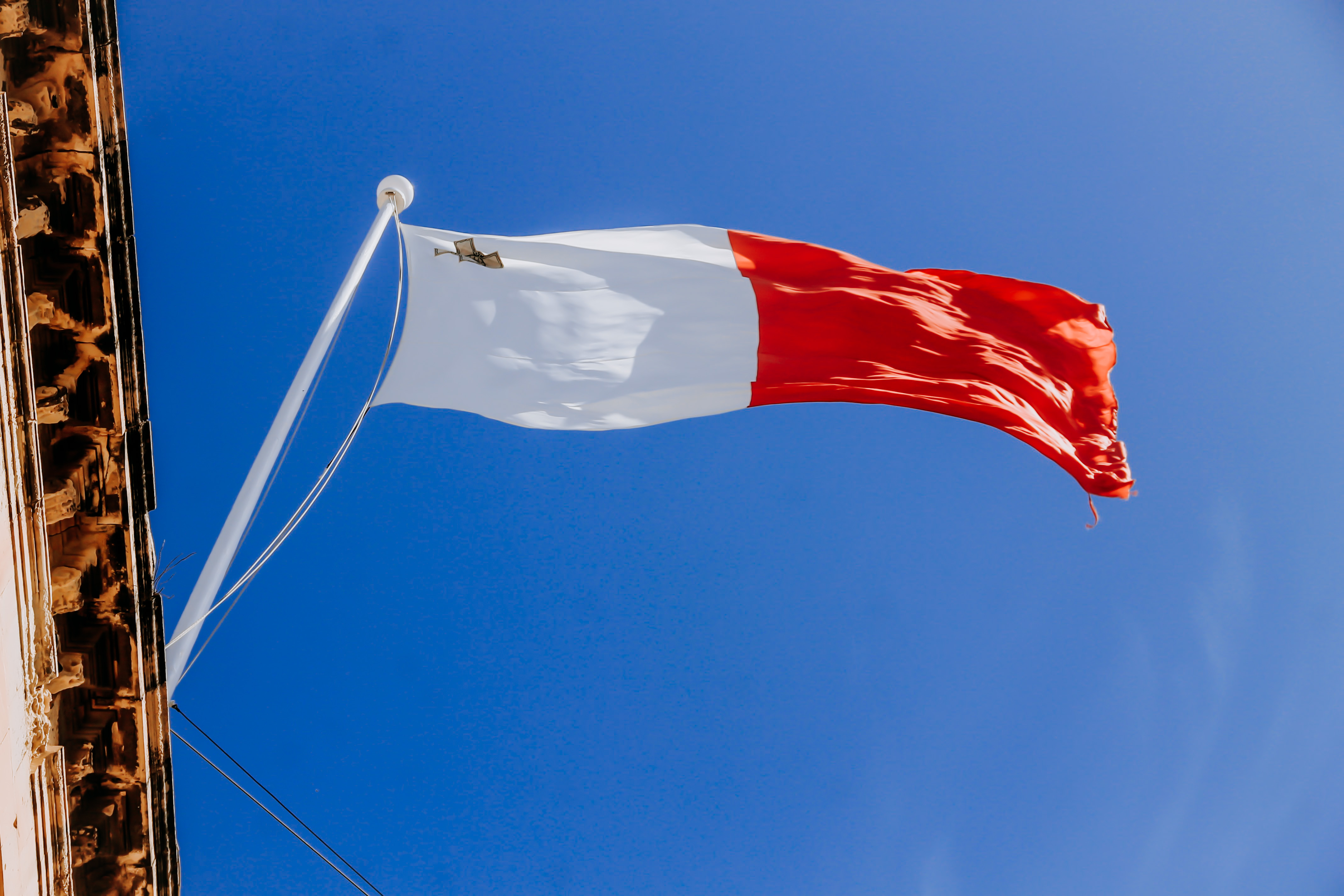 Malta flag waving against a clear blue sky, showing white, red, and George Cross.
