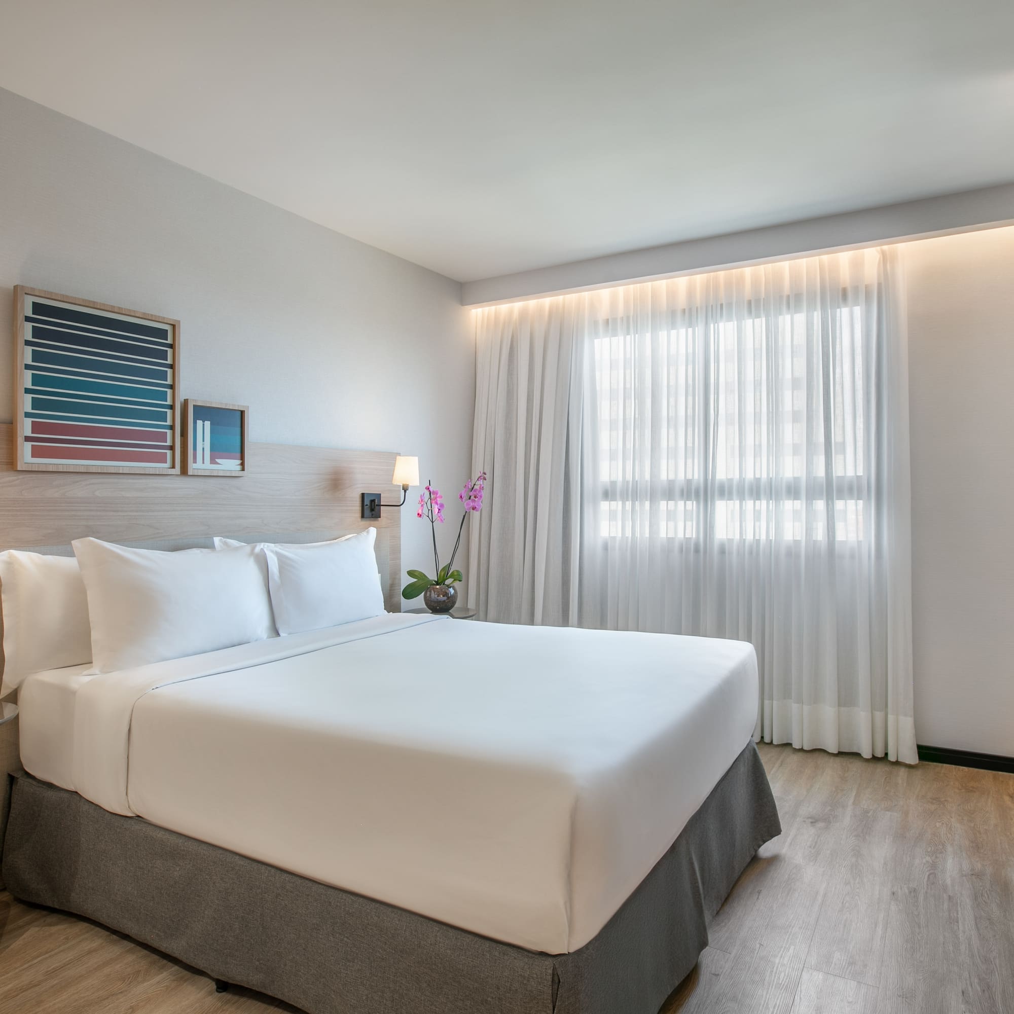 Modern hotel room with king bed, white bedding, wood accents, and window.