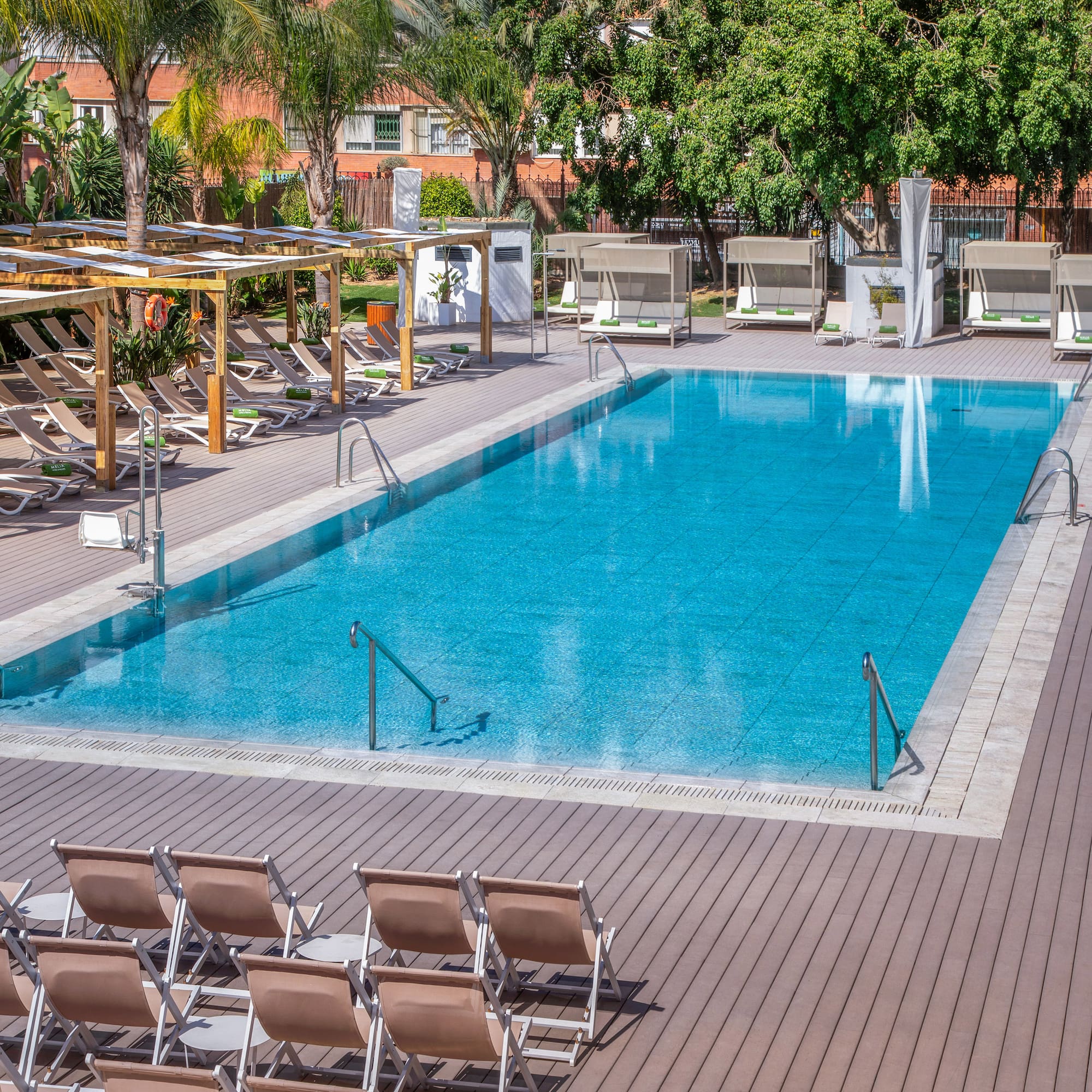 Resort swimming pool with sun loungers, shaded areas, and tropical trees.