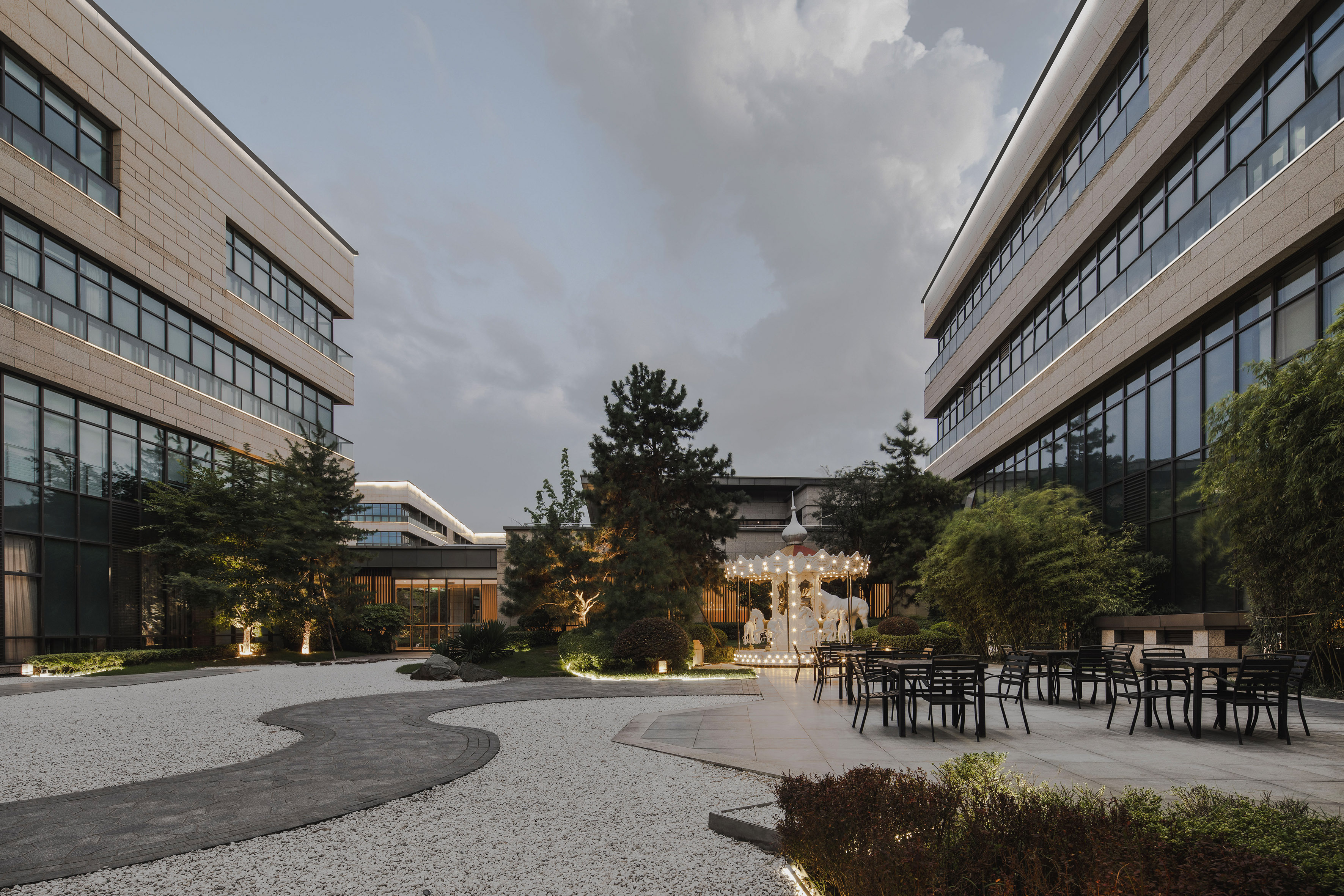 Modern building courtyard, illuminated carousel, outdoor dining at dusk.