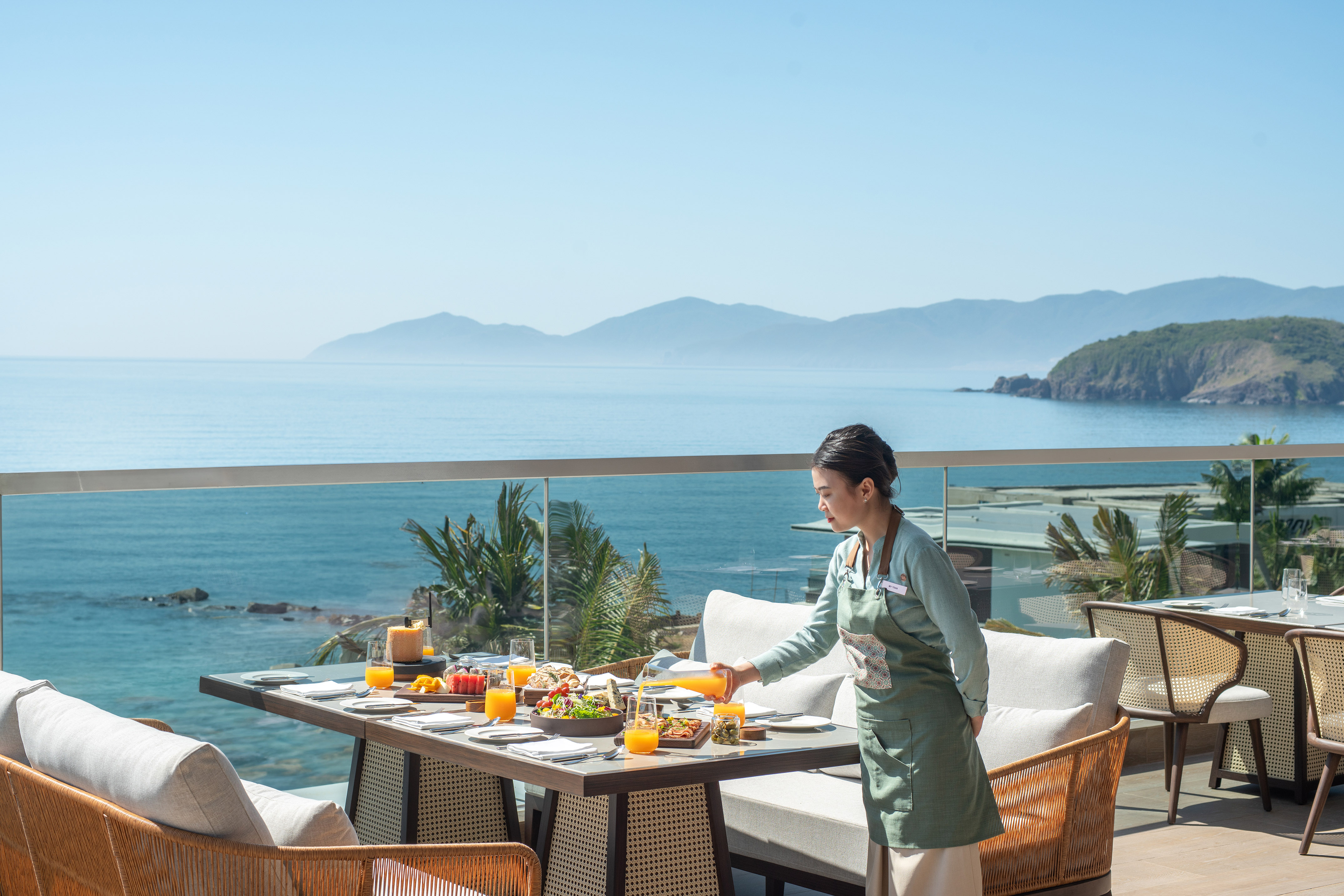 Server pouring juice at an outdoor breakfast table with ocean view.