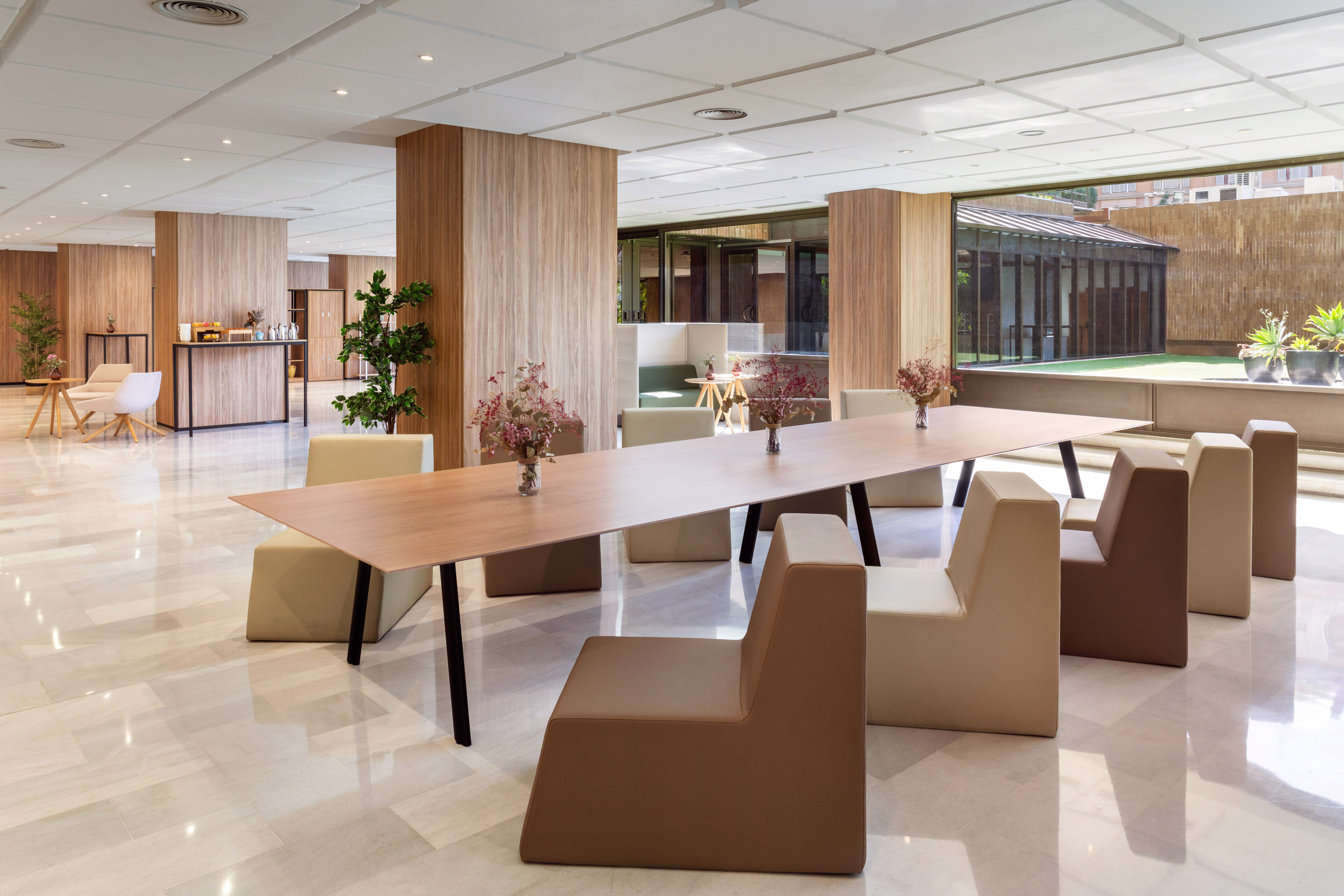 Modern hotel lounge with long communal table, stylish seating, and garden view.