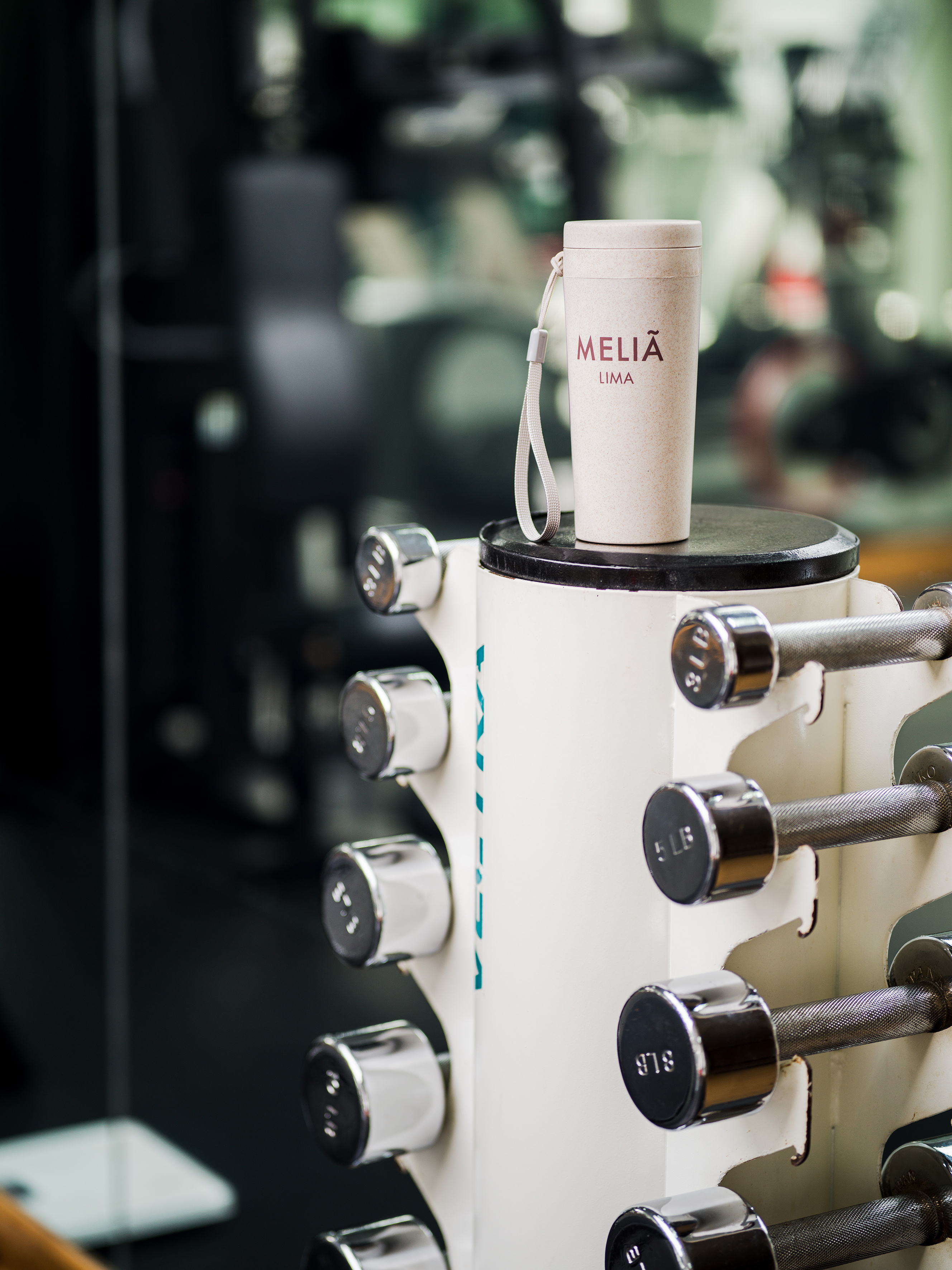 Melia Lima branded reusable tumbler on a dumbbell rack at a hotel gym.