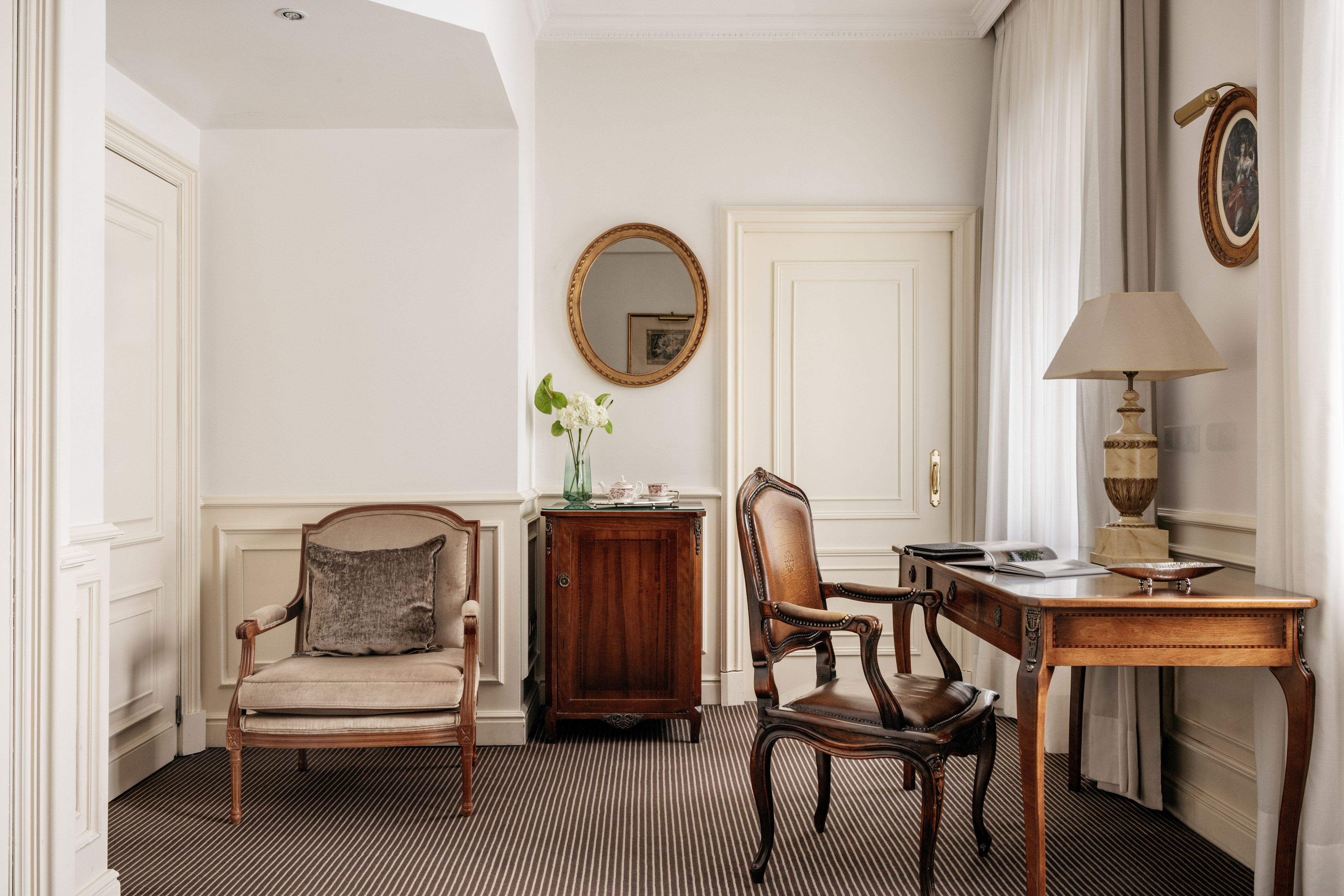 Classic luxury hotel suite with ornate desk, leather chair, and armchair.