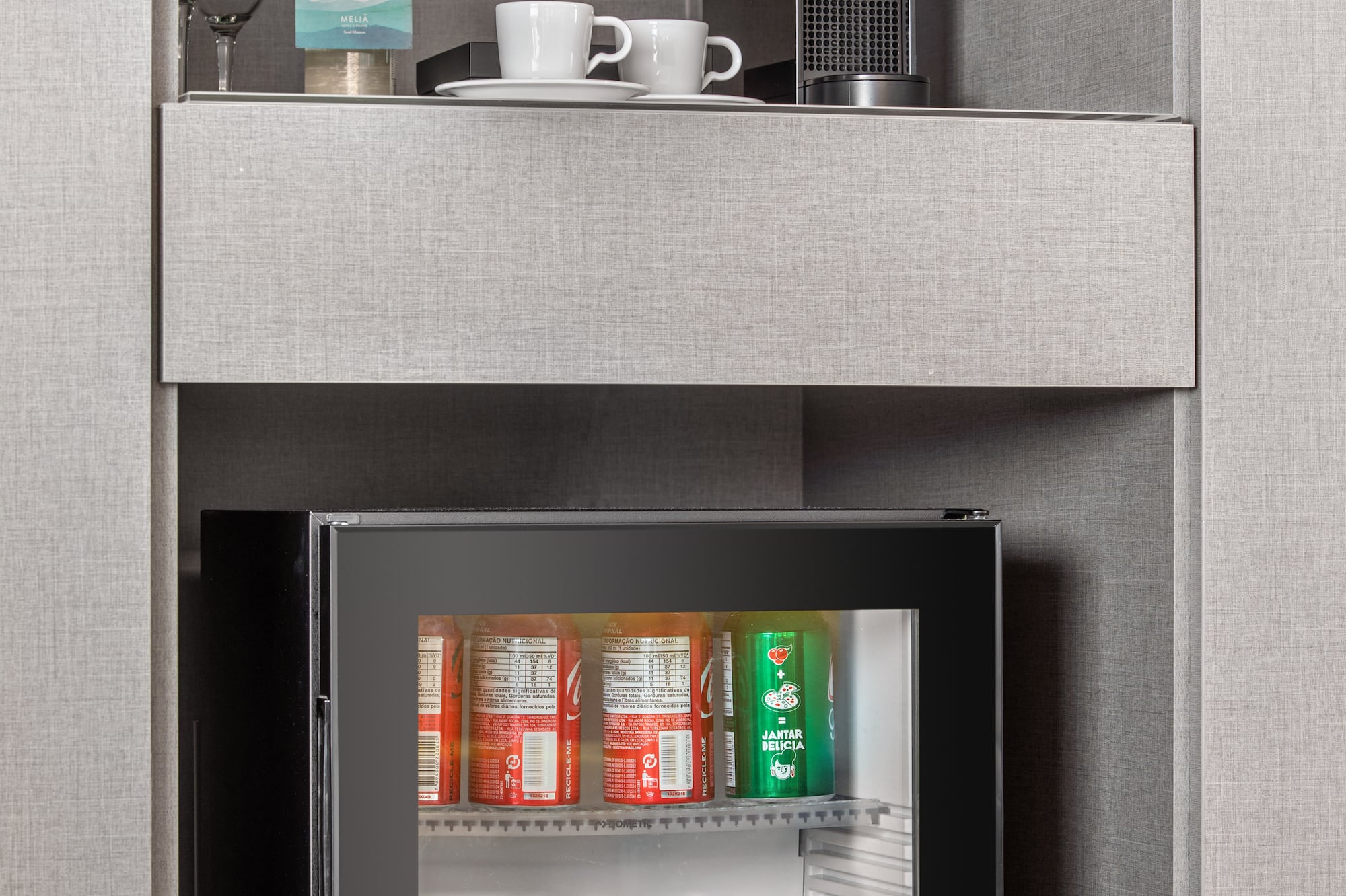 a small refrigerator with drinks and cups on top of it