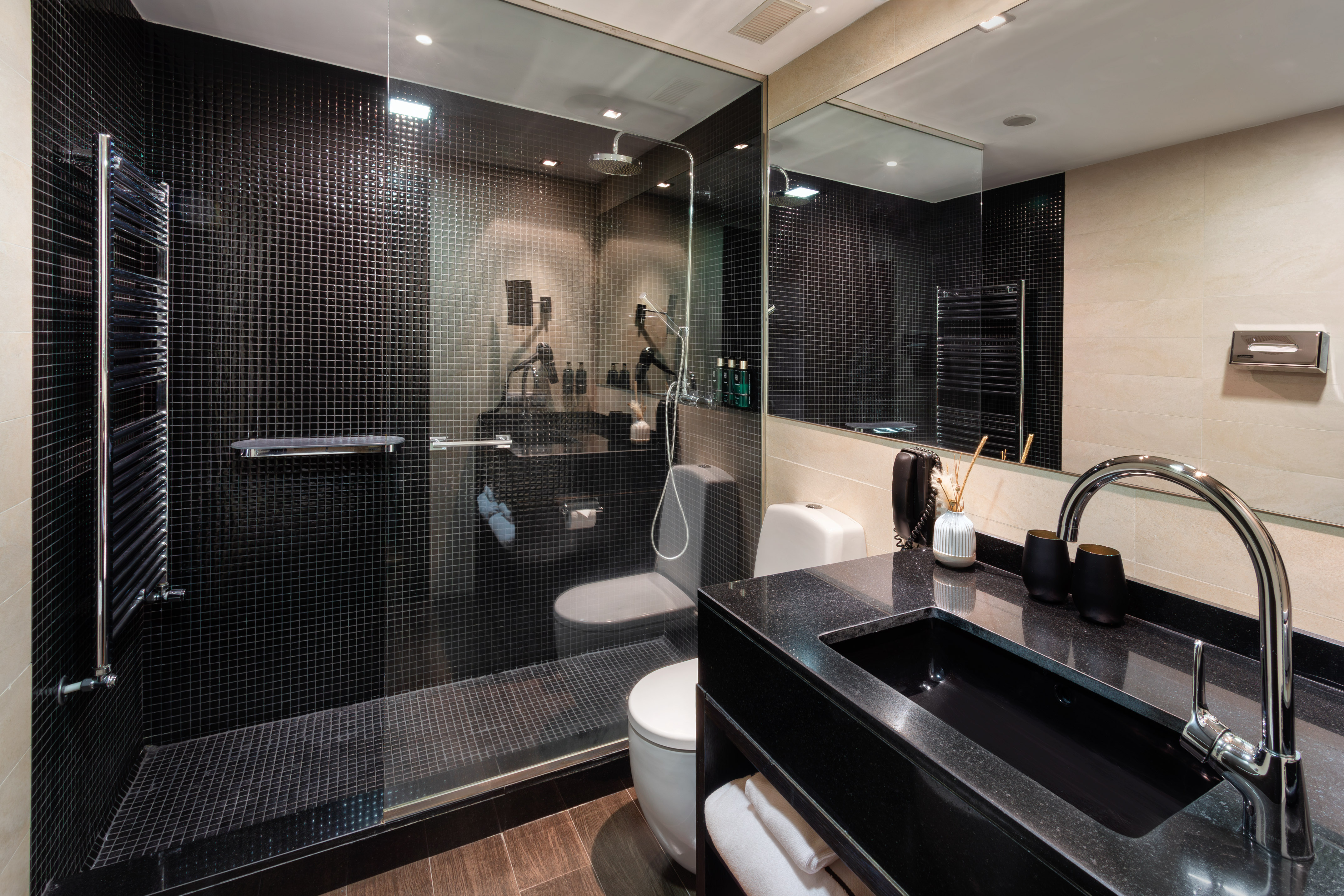 Modern bathroom with black mosaic tiled shower, toilet, and granite vanity.