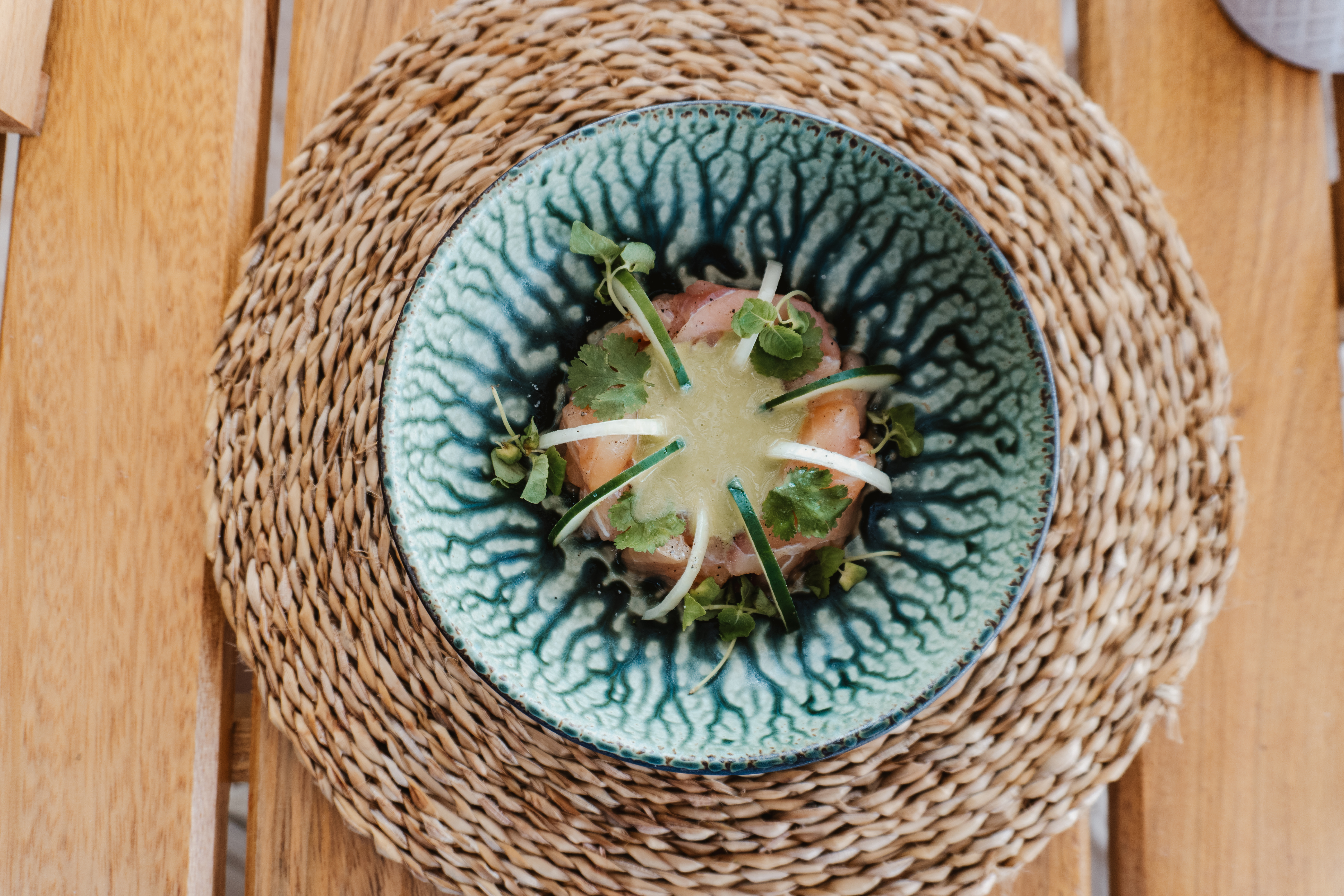 Teal bowl of fresh fish crudo with green sauce, cucumber, and herbs.