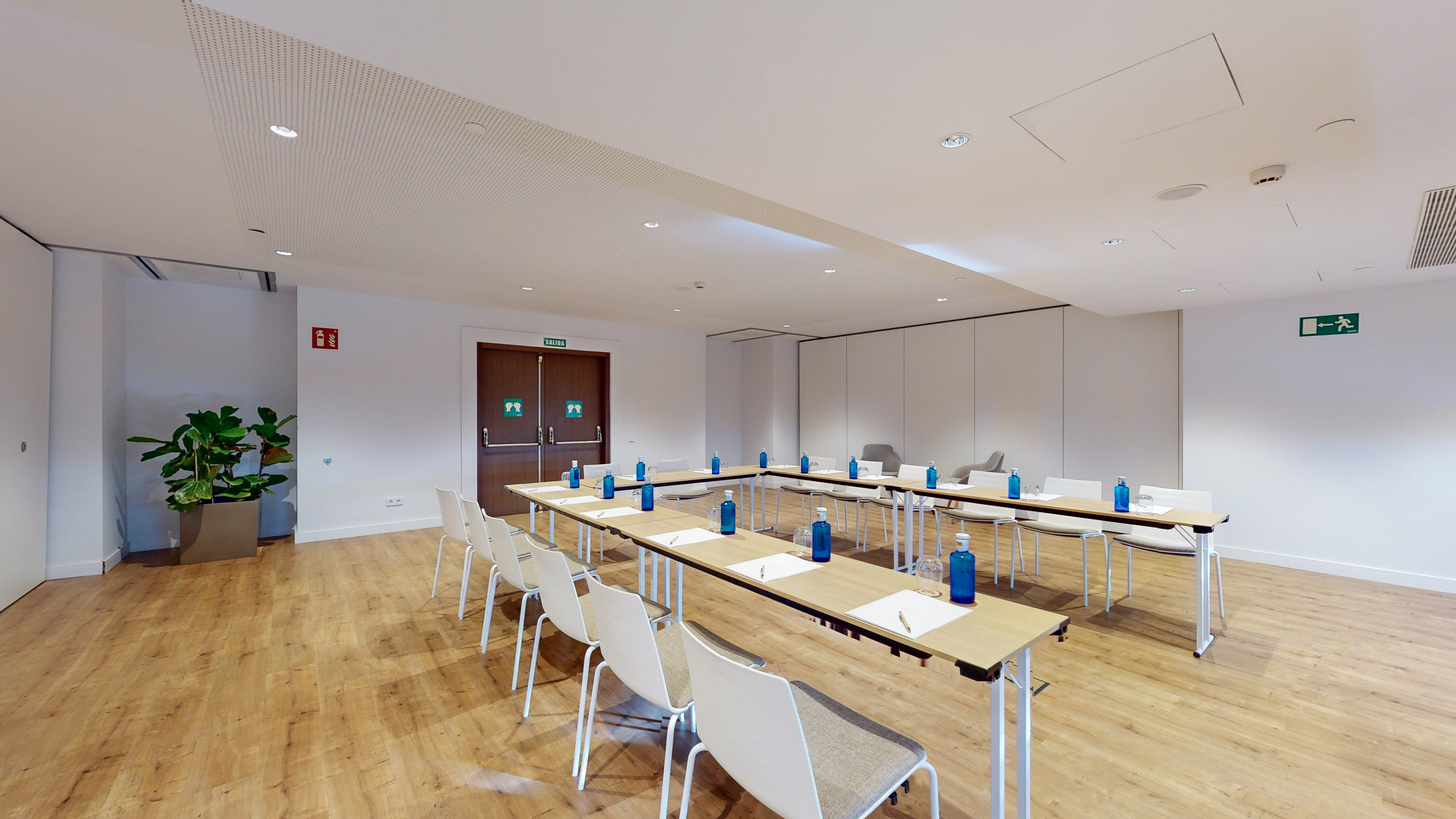 Modern conference room with U-shaped tables, chairs, wood floor.