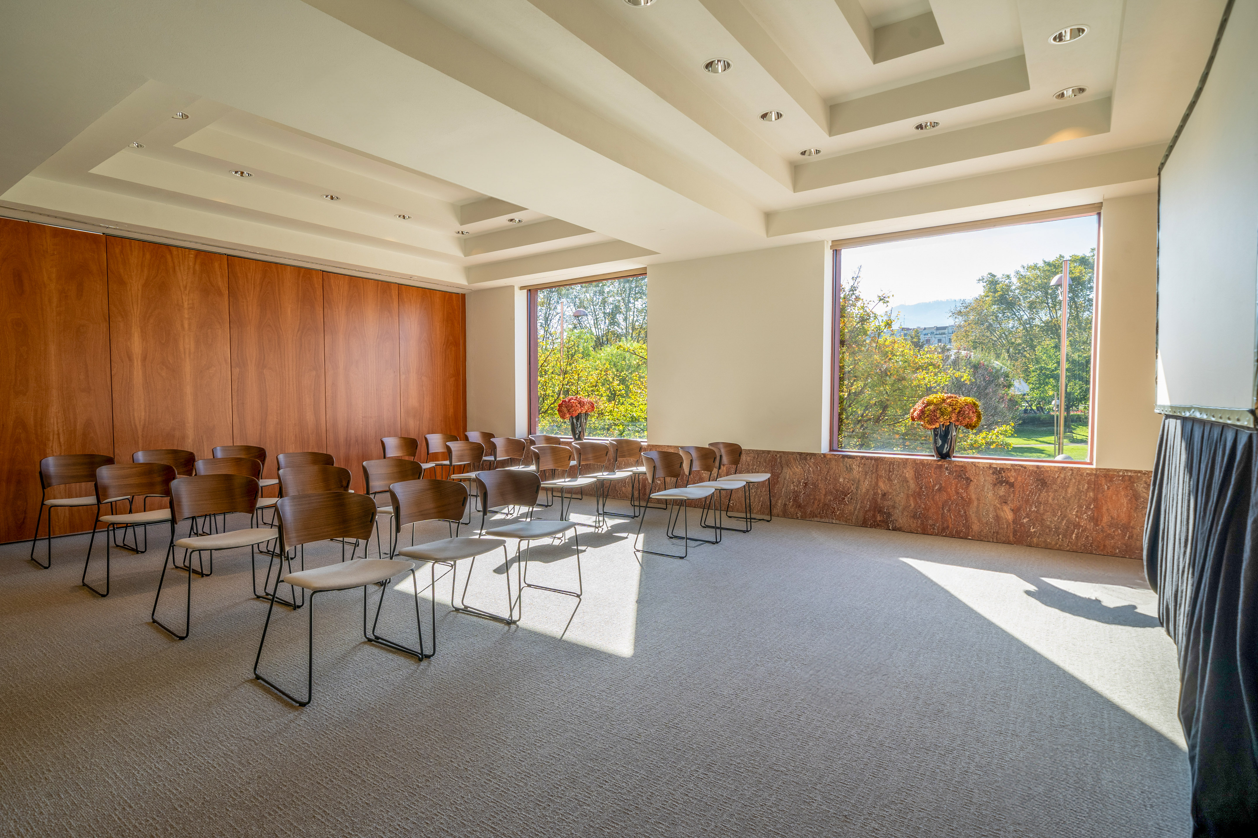 Modern conference room with rows of chairs, large windows, and natural light.