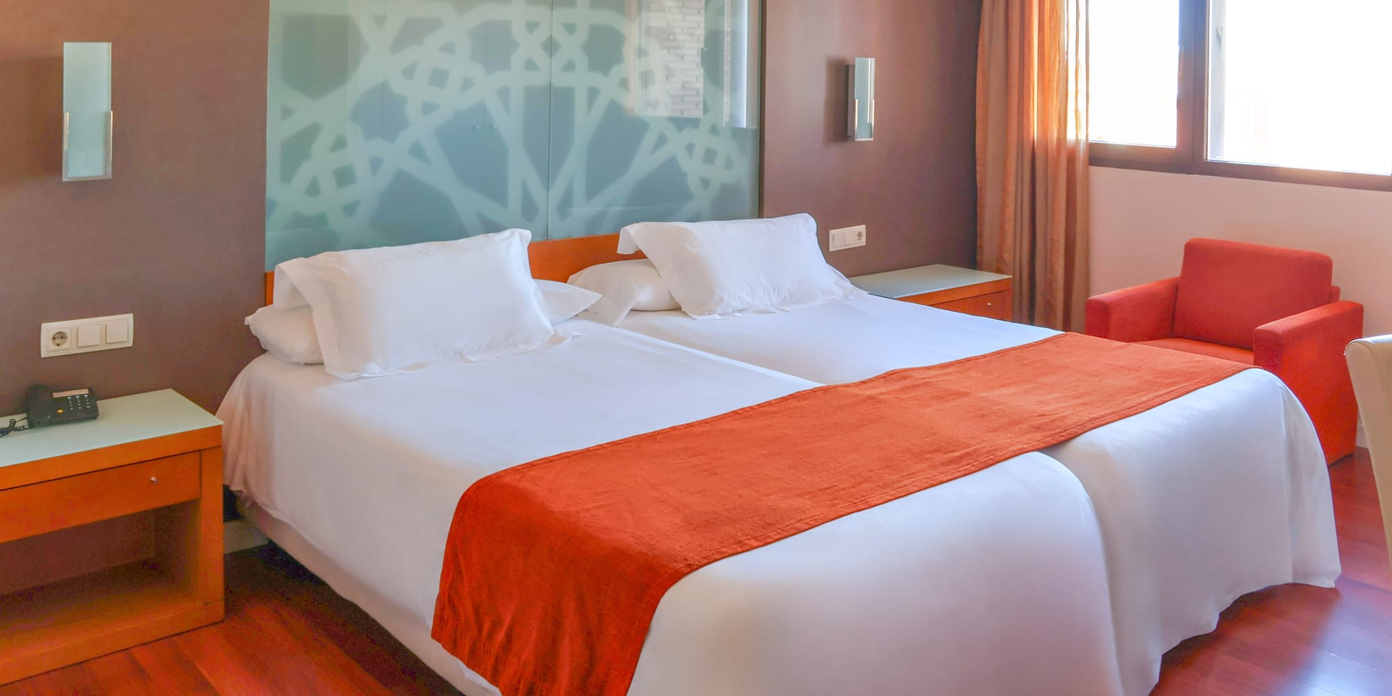 Modern hotel room with two single beds, white linen, and orange accents.